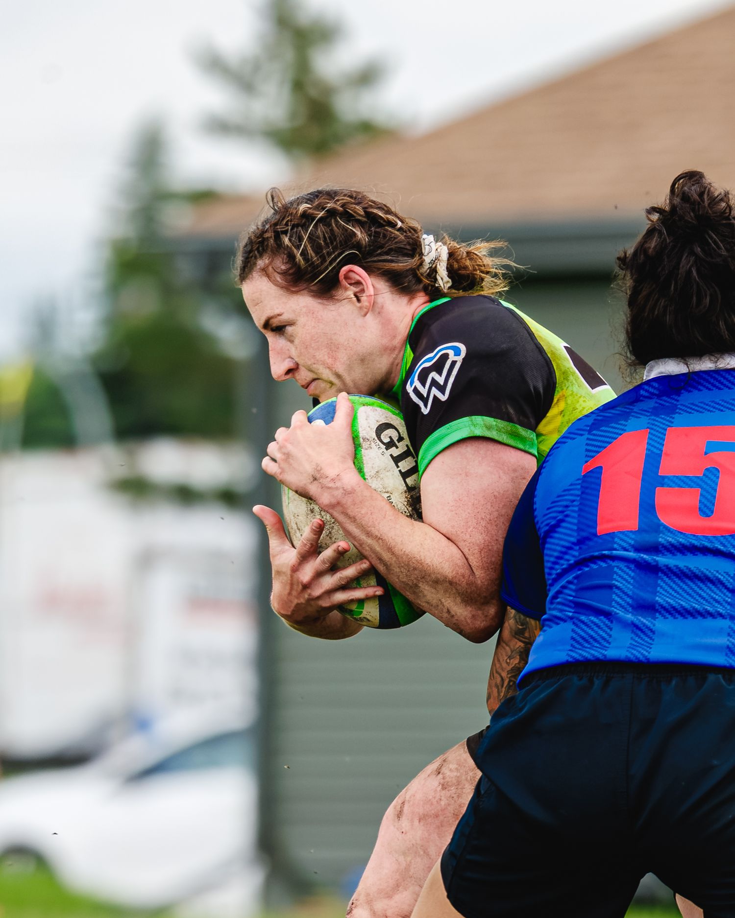 Women's rugby player in green and black jersey drives forward with ball during intense match.