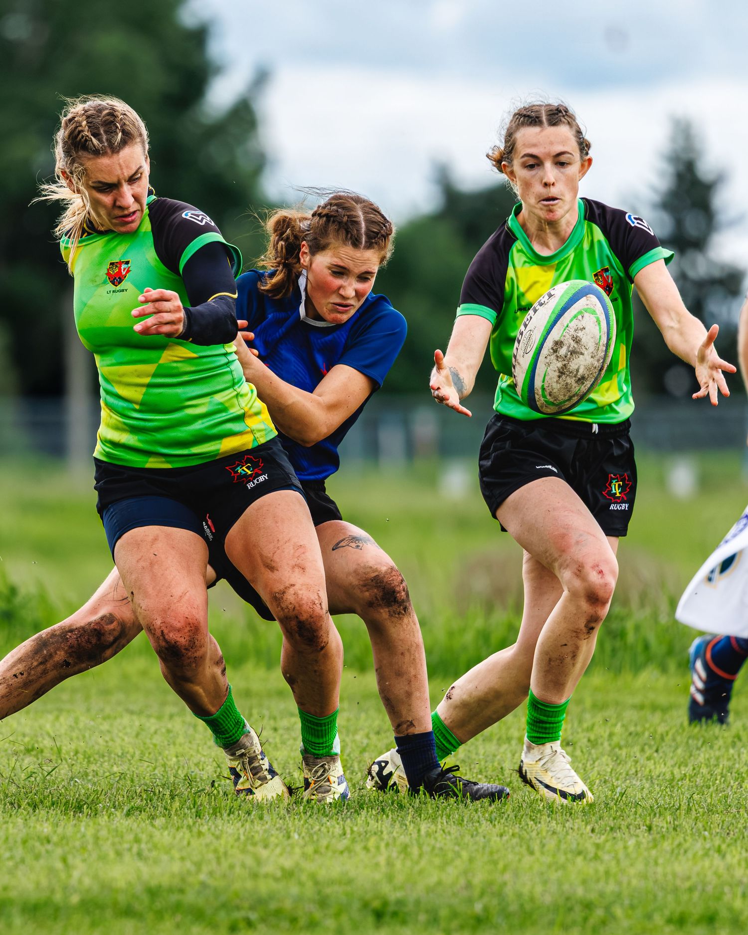 Women rugby players in green jerseys compete for the ball during a muddy match on a grass field.