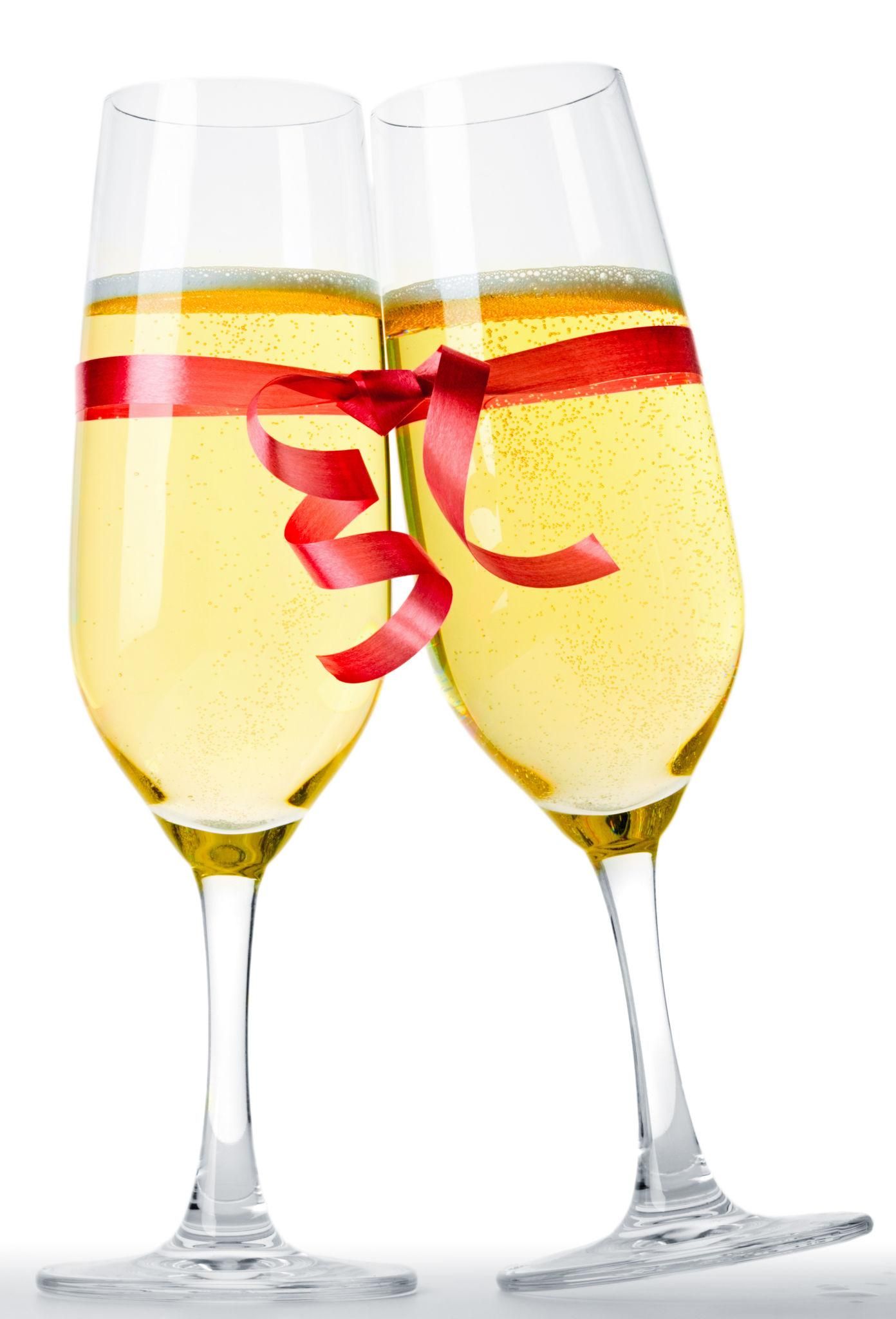Two champagne flutes filled with sparkling wine tied together with a red ribbon bow on white background.
