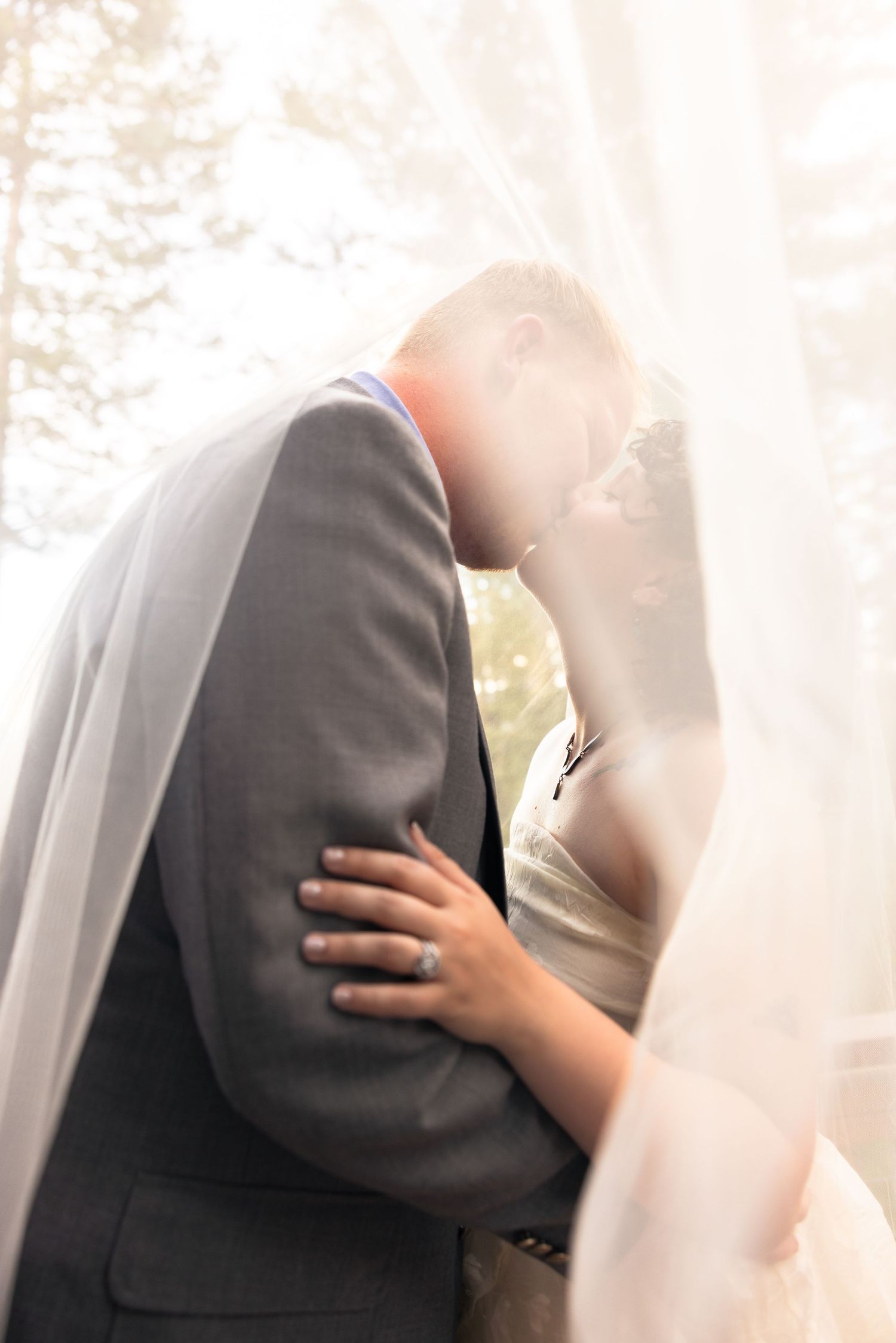 Bride and groom sharing a romantic kiss under a flowing white veil on their wedding day.