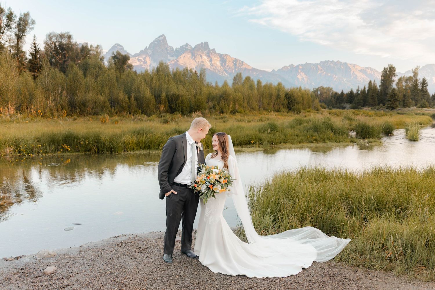Bride and groom share a romantic moment by a mountain river in Grand Teton National Park at golden hour.