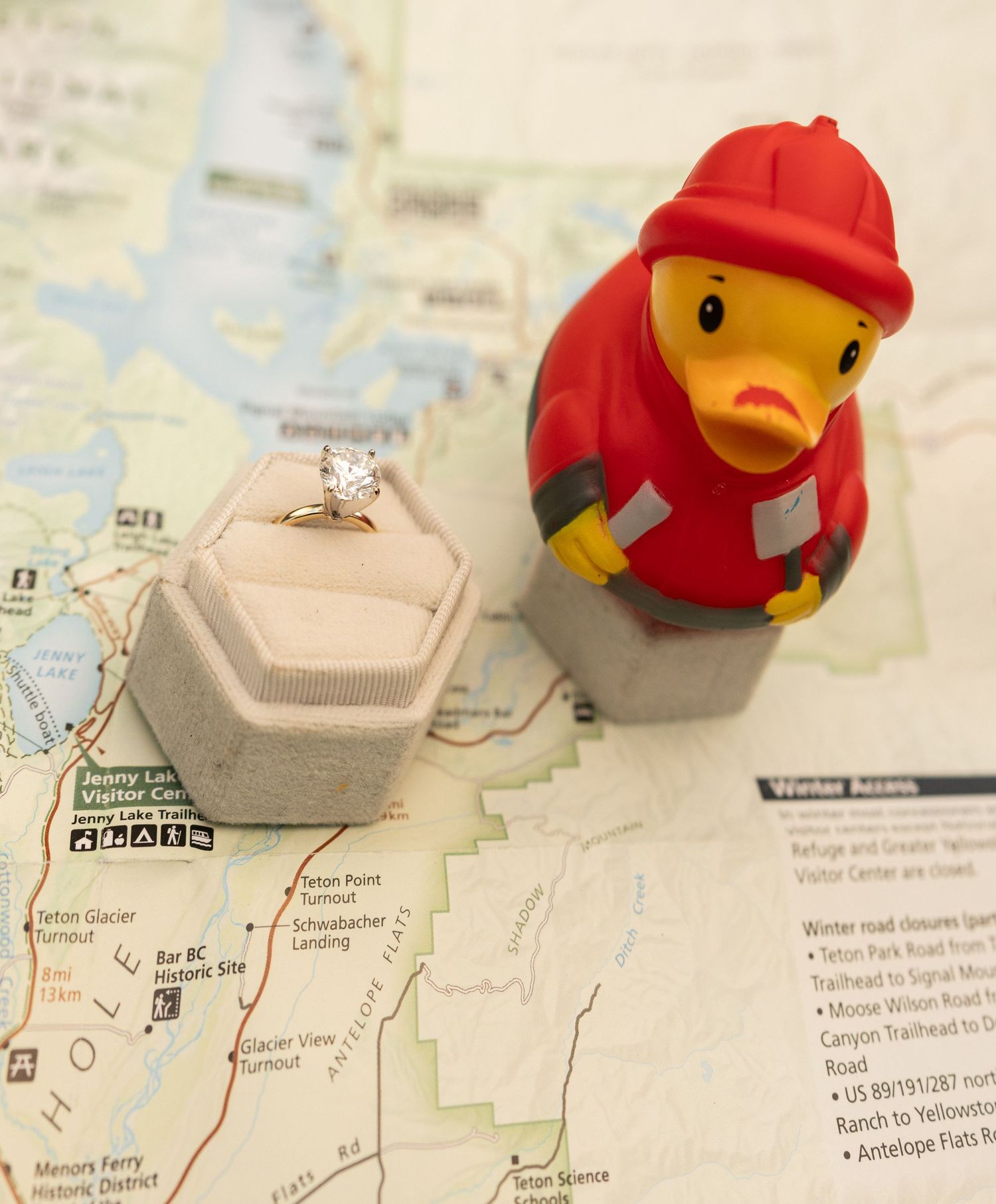 Rubber duck firefighter toy beside a diamond engagement ring in a velvet box on a Yellowstone map.