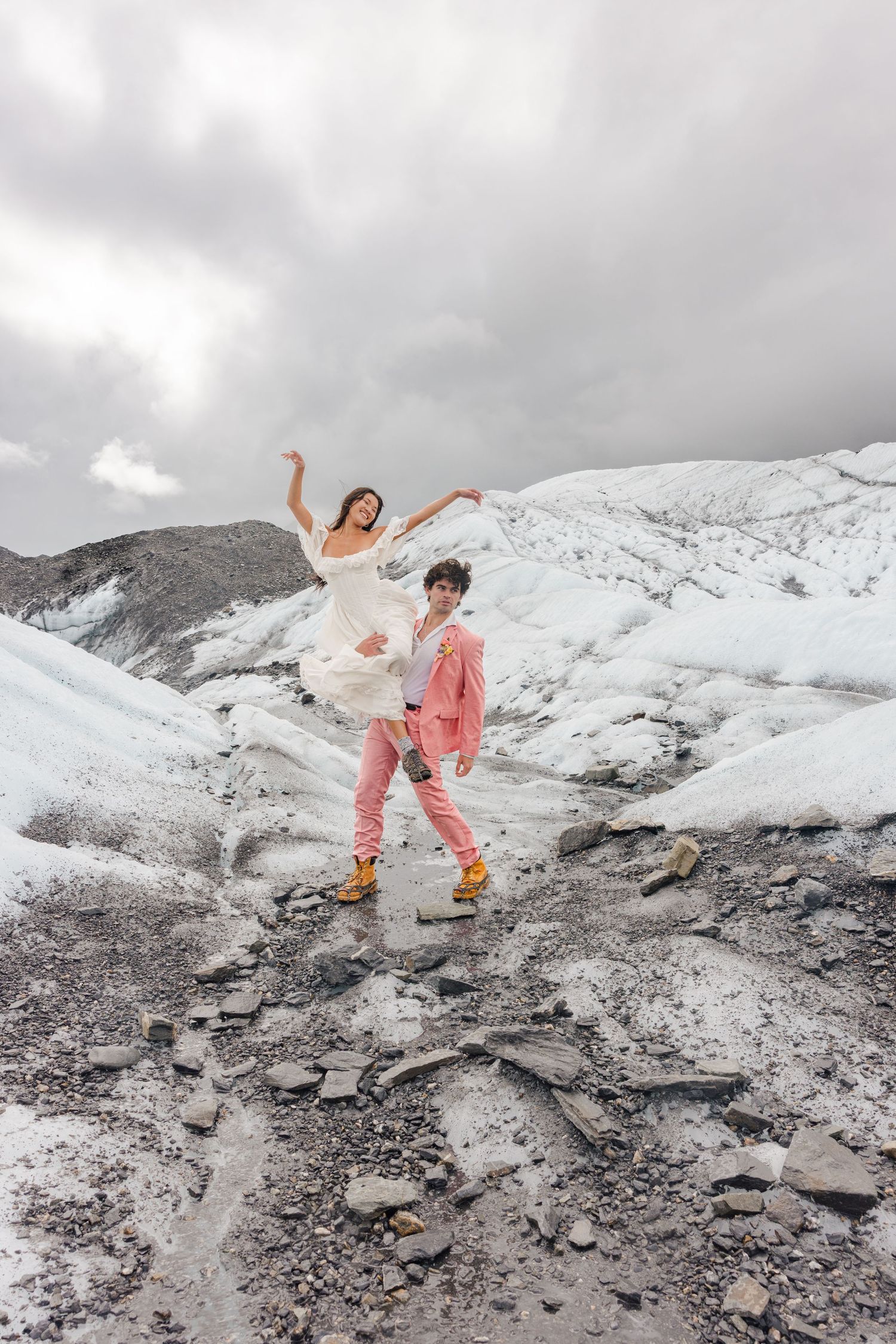 Couple in wedding attire dancing for their adventure bridal photos on a glacier in Alaska.