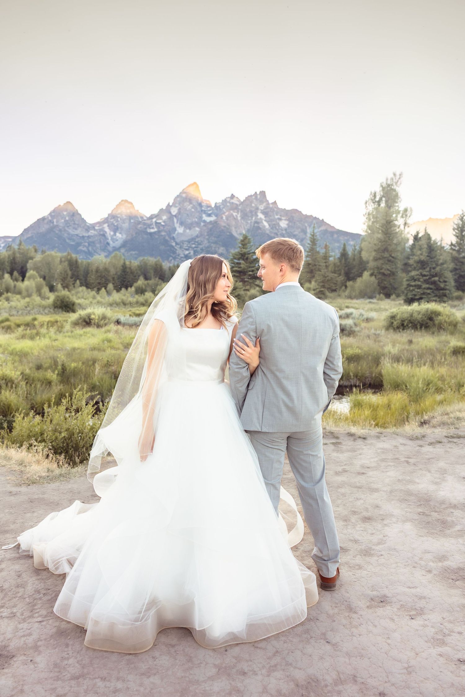 Bride and groom embracing with Grand Teton mountains backdrop at sunset wedding photo.
