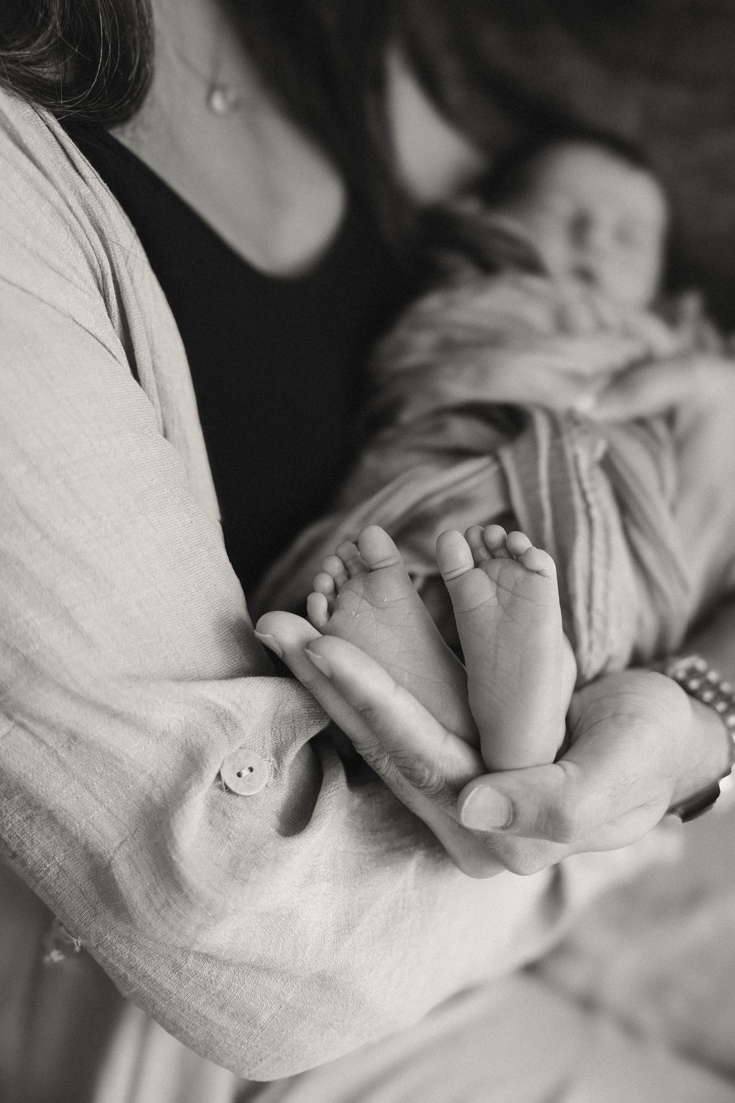 Black and white photo of a mother cradling her newborn baby, gently holding the infant's tiny feet in her hands.