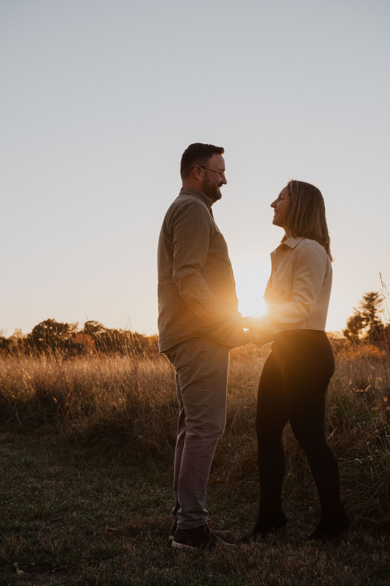 Couple holding hands and laughing together in a golden field at sunset.