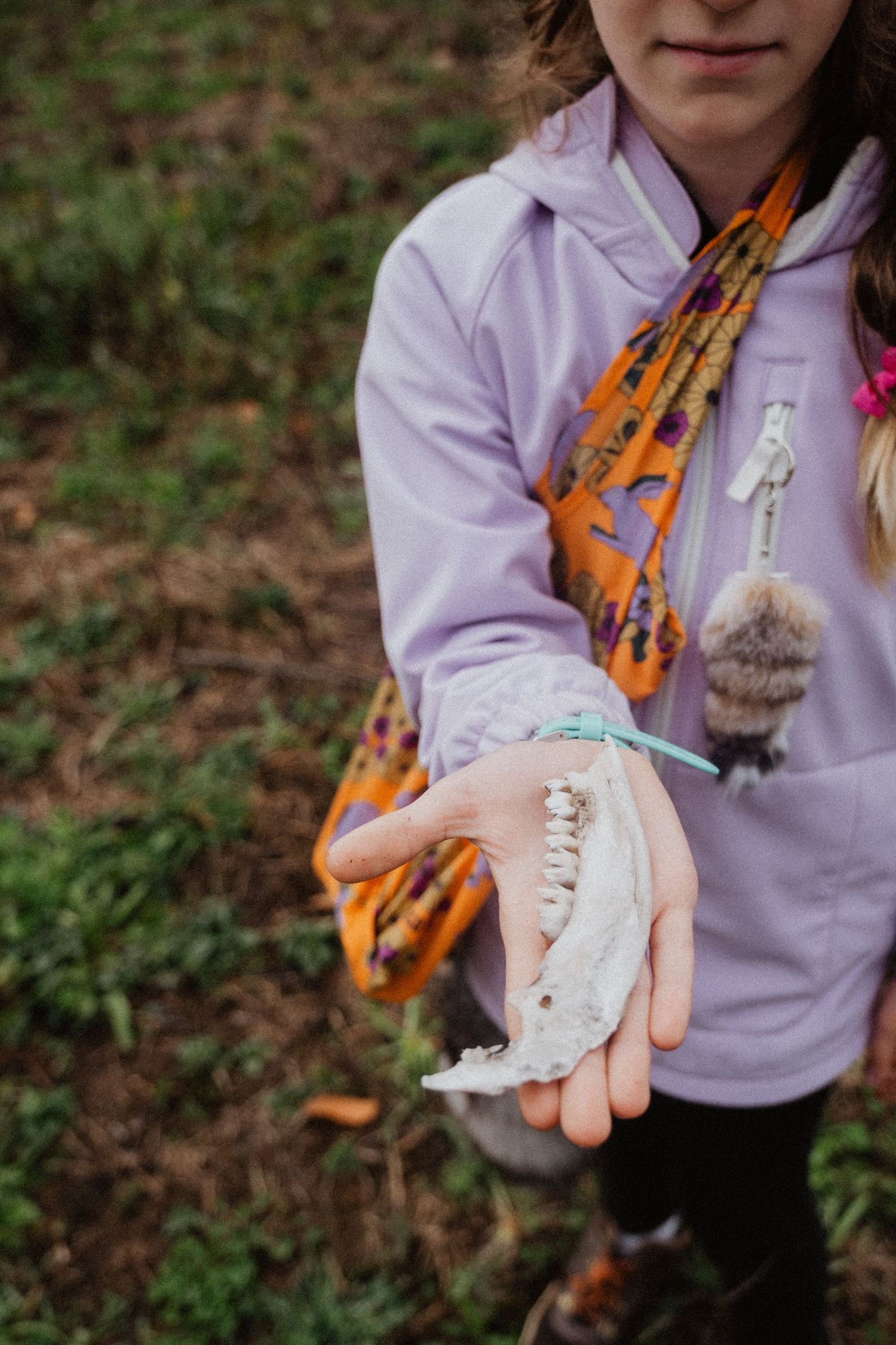 Girl in purple hoodie holds an animal jaw bone outdoors in a grassy field.