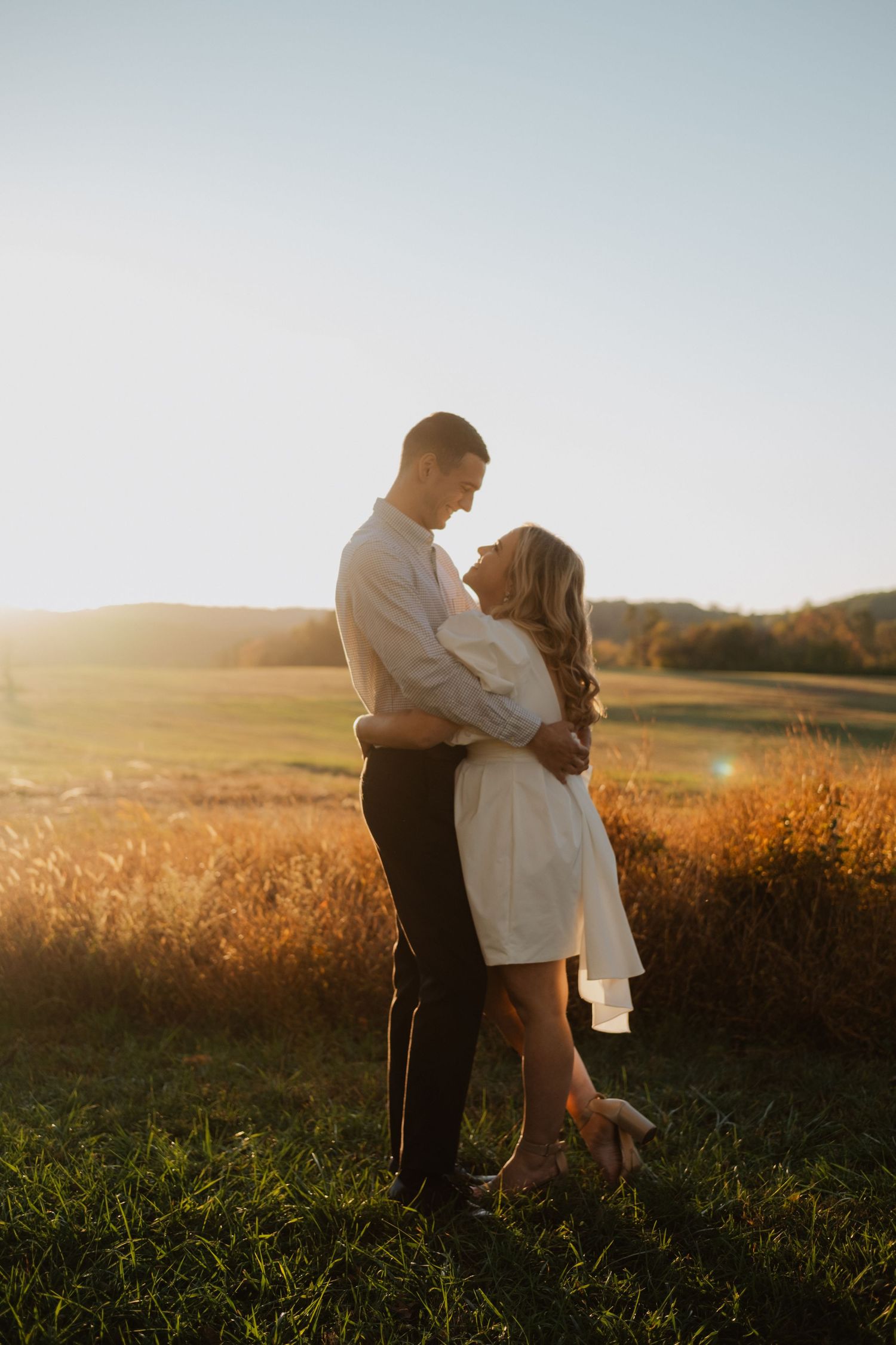 Couple embracing at golden hour in a sunlit field at sunset.