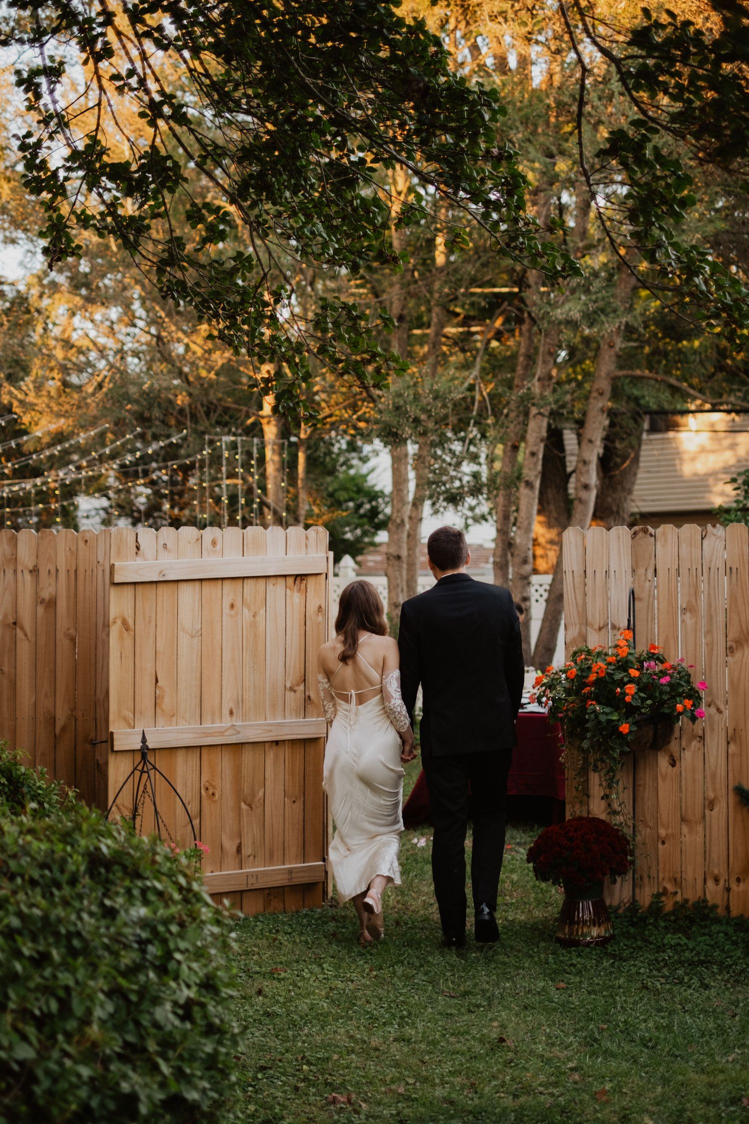 Bride and groom walking hand in hand through a garden with string lights.