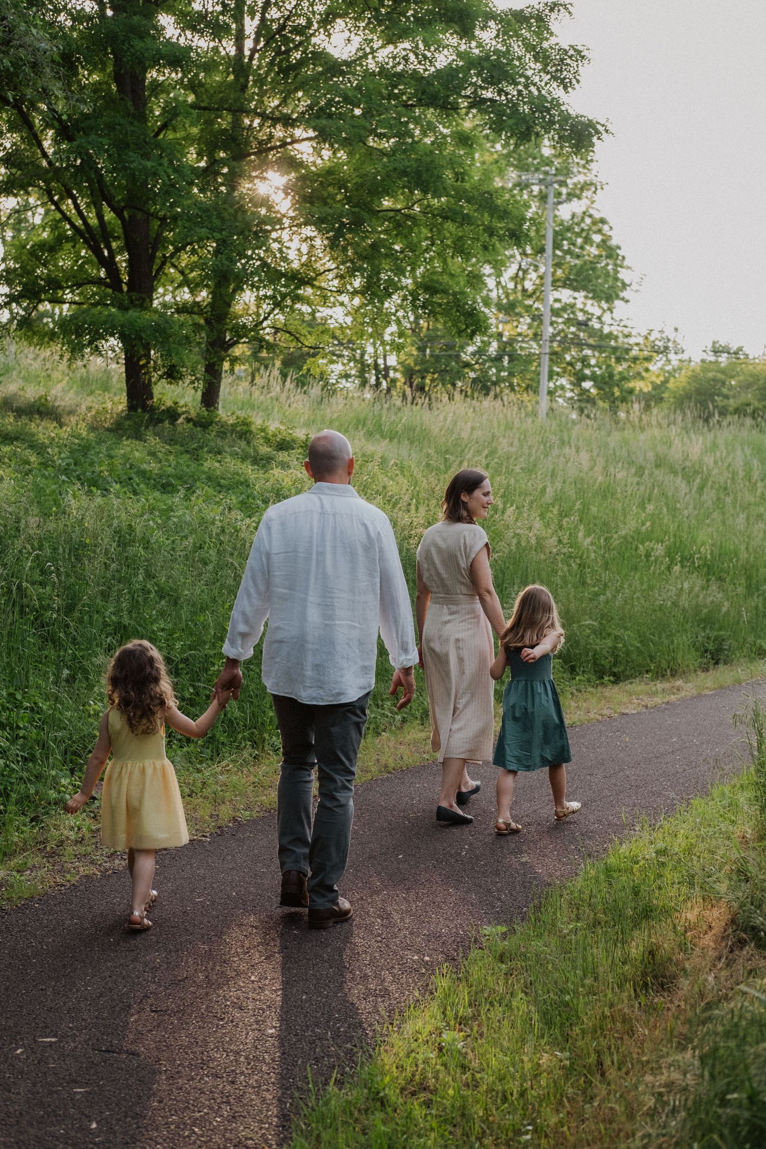 Family of four holding hands on a paved path surrounded by greenery.