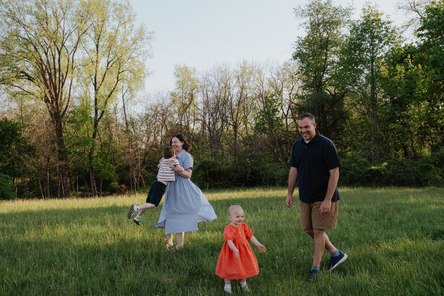 Happy family with two children playing in a sunny green meadow during golden hour.