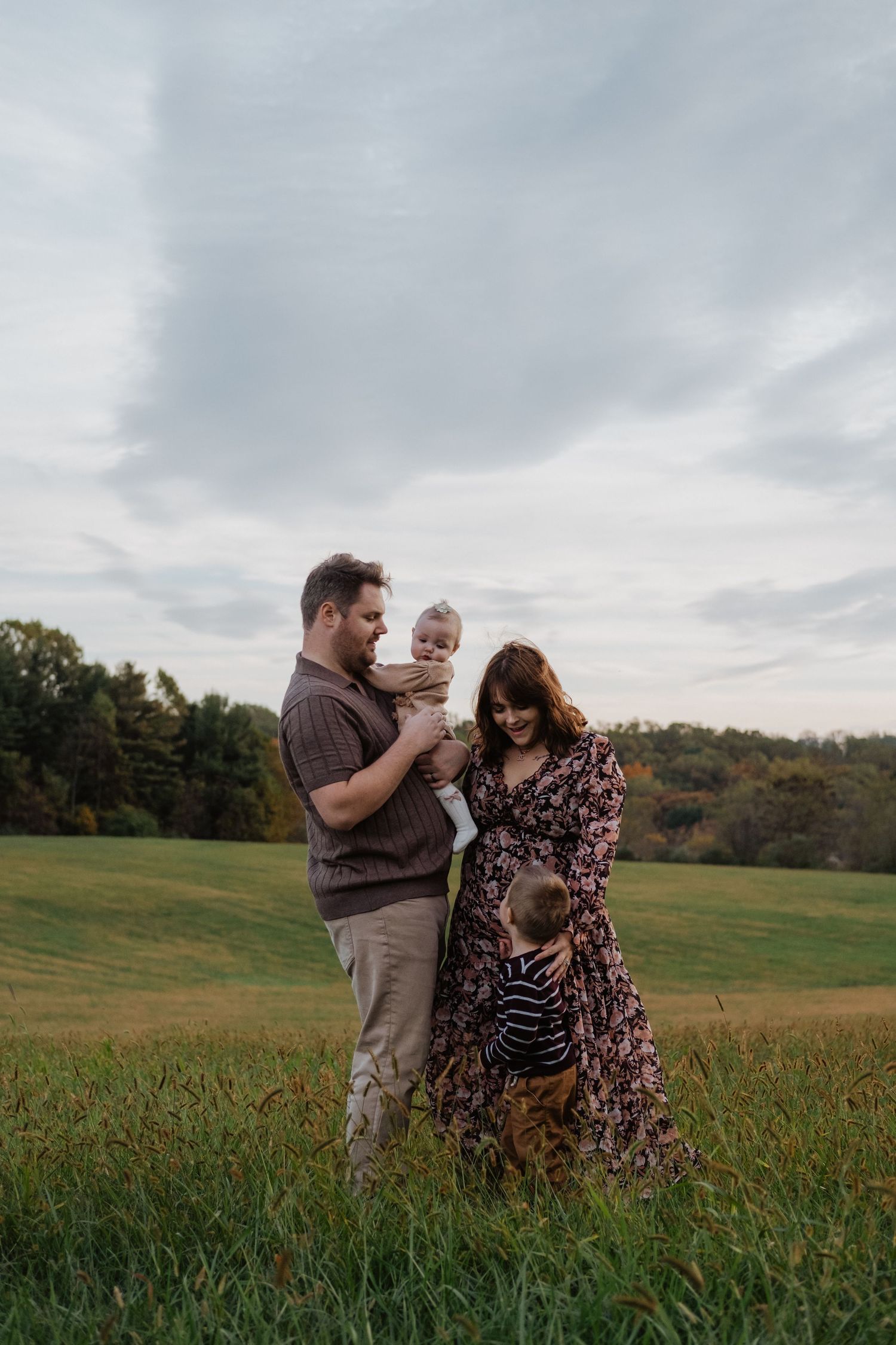 Young family of four enjoying outdoor fall portrait session in green meadow at dusk.
