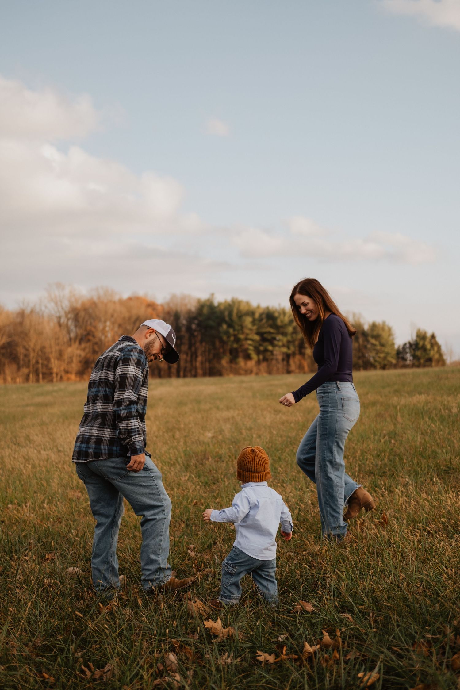 Young family with a toddler playing together in an autumn field at golden hour.