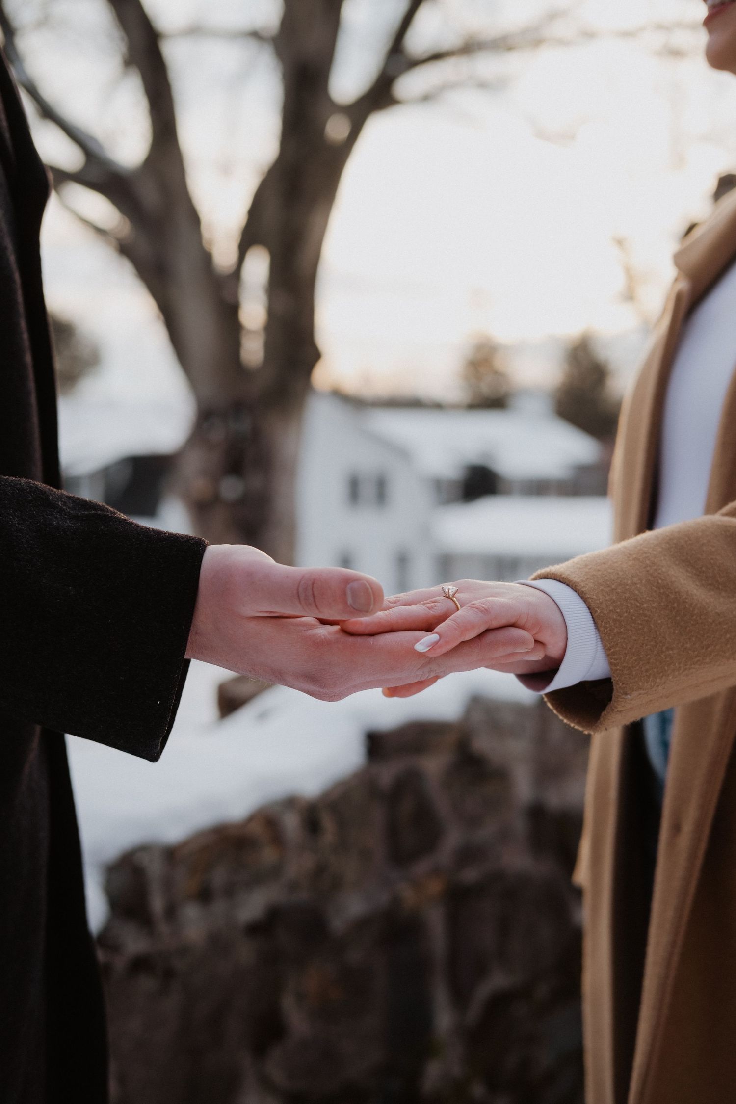 Close-up of couple holding hands gently outdoors in winter, with snowy rocky background at dusk.