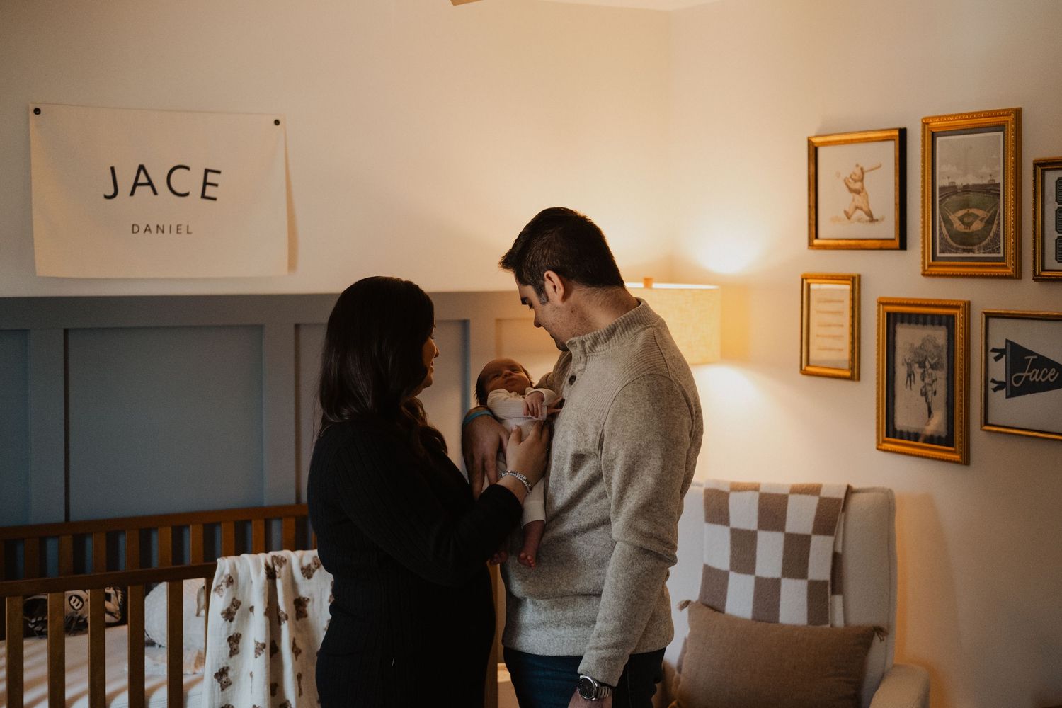 Parents admiring newborn baby in nursery with Jace Daniel name sign above blue crib in warm cozy room.