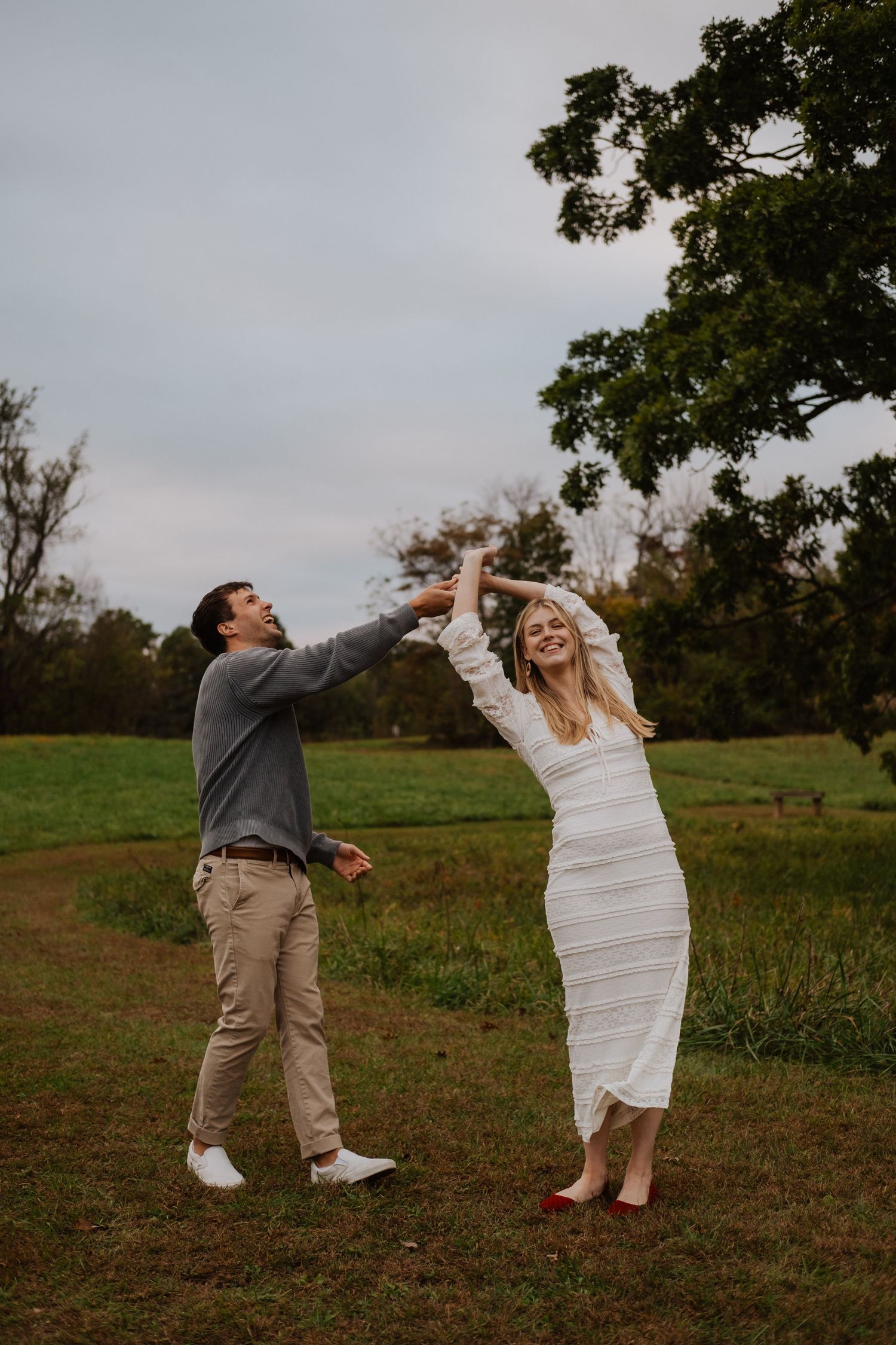 Couple dancing and spinning joyfully in a green field on a cloudy day.