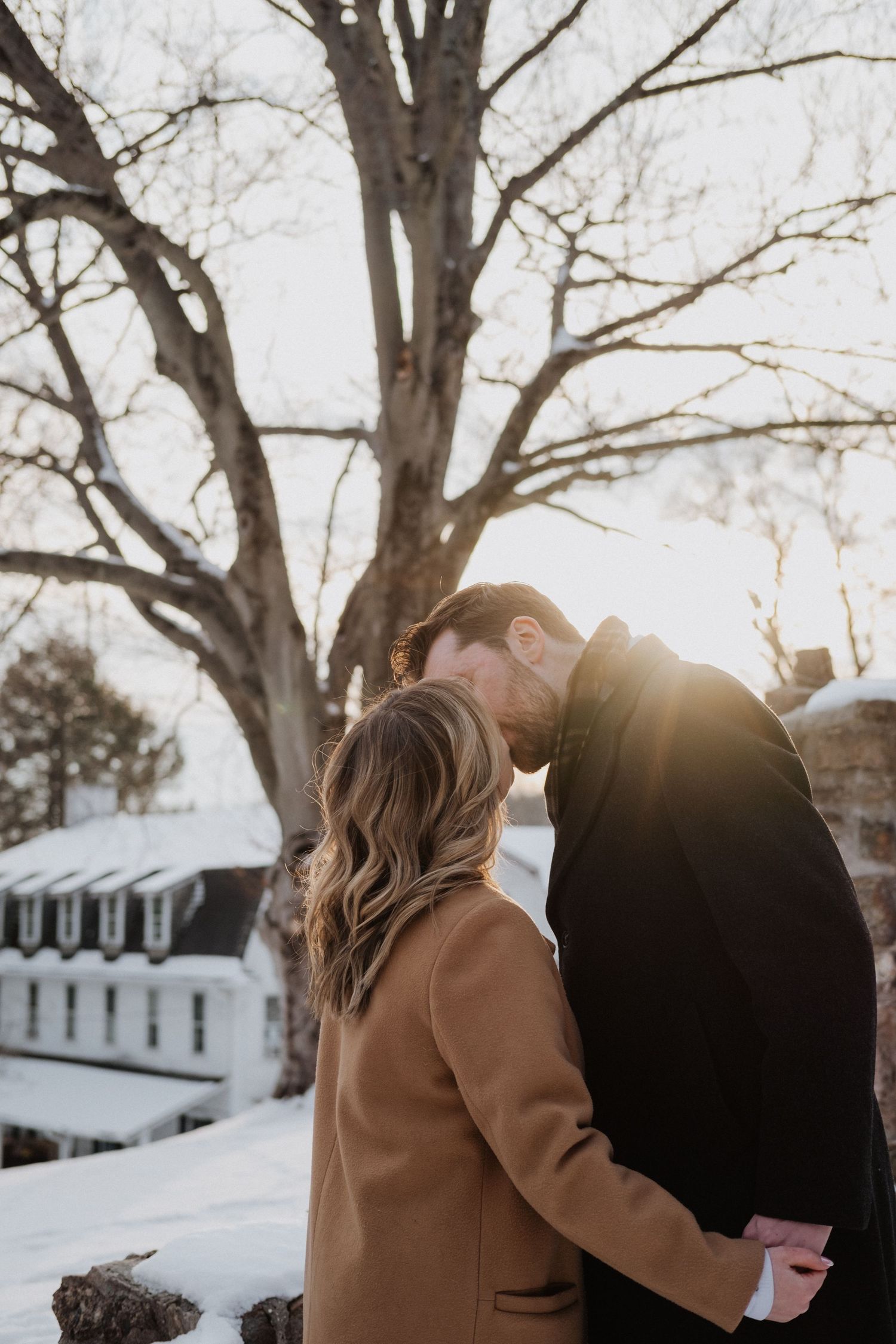 Couple sharing an intimate moment at golden hour in winter, leaning foreheads together in snowy setting.