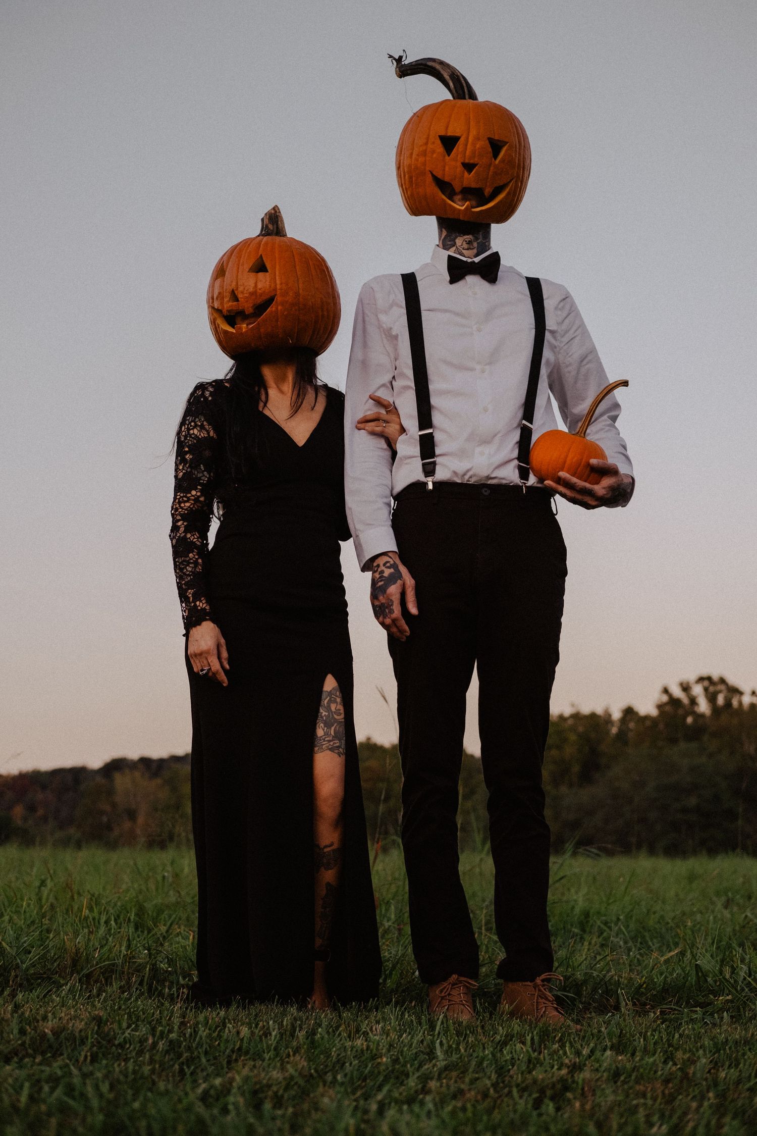 Couple wearing jack-o-lantern pumpkin heads standing in a field at dusk.