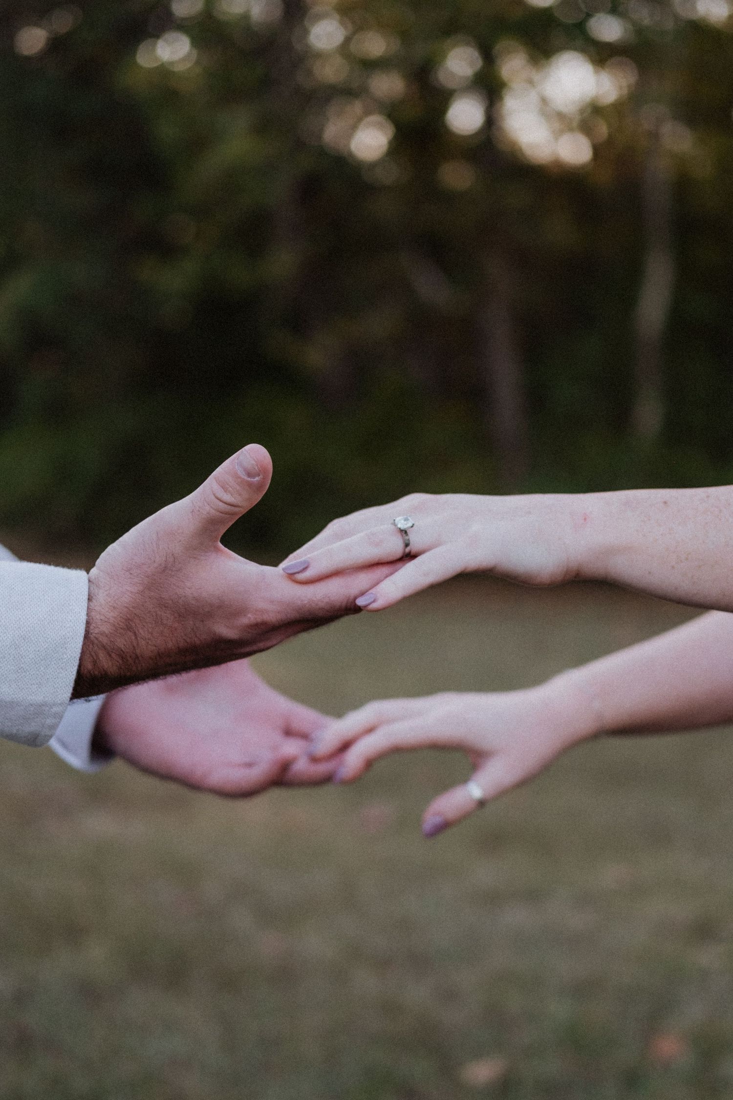 Close-up of couple reaching hands, woman wearing an engagement ring outdoors.
