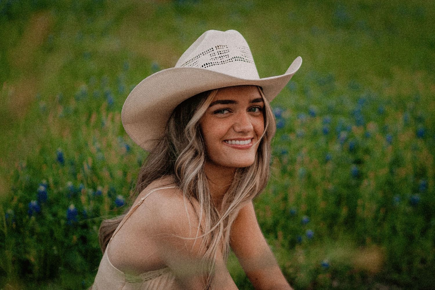 Smiling young woman wearing a white cowboy hat in a field of blue wildflowers.