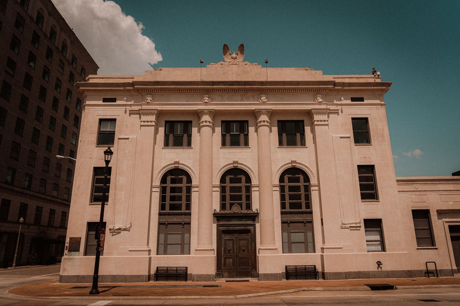 Historic neoclassical building with arched windows and ornate facade on a city street corner under a blue sky.