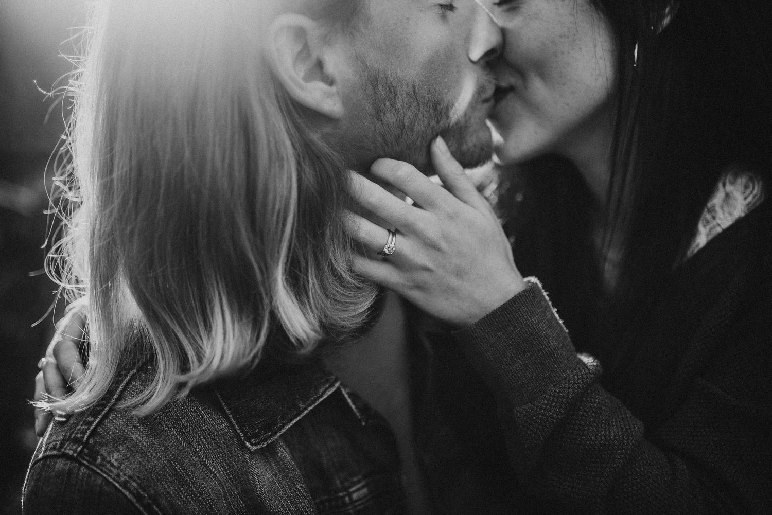 Black and white photo of a couple sharing a romantic kiss, woman wearing an engagement ring.