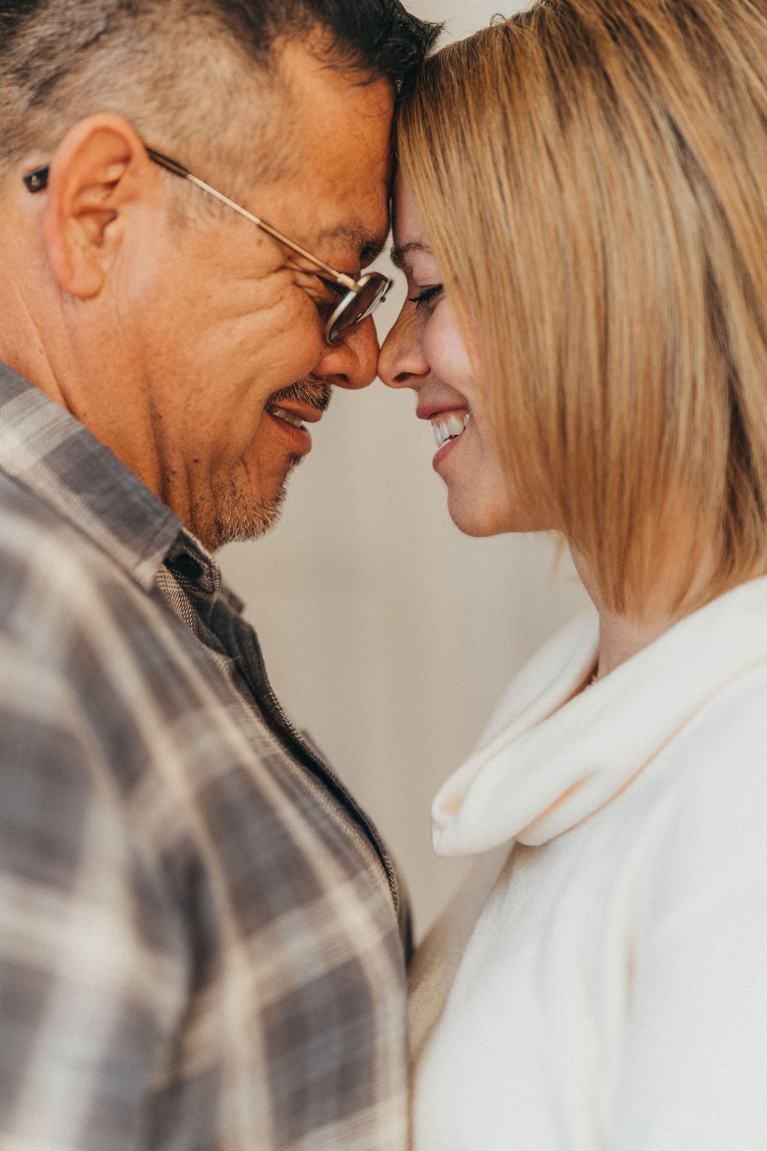 A middle-aged couple in glasses smile and touch foreheads in a romantic and tender moment.