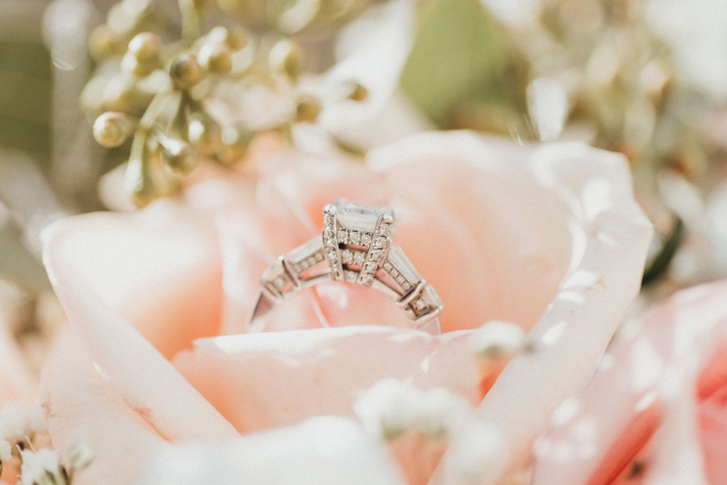 Princess-cut diamond engagement ring nestled in a soft pink rose bloom.