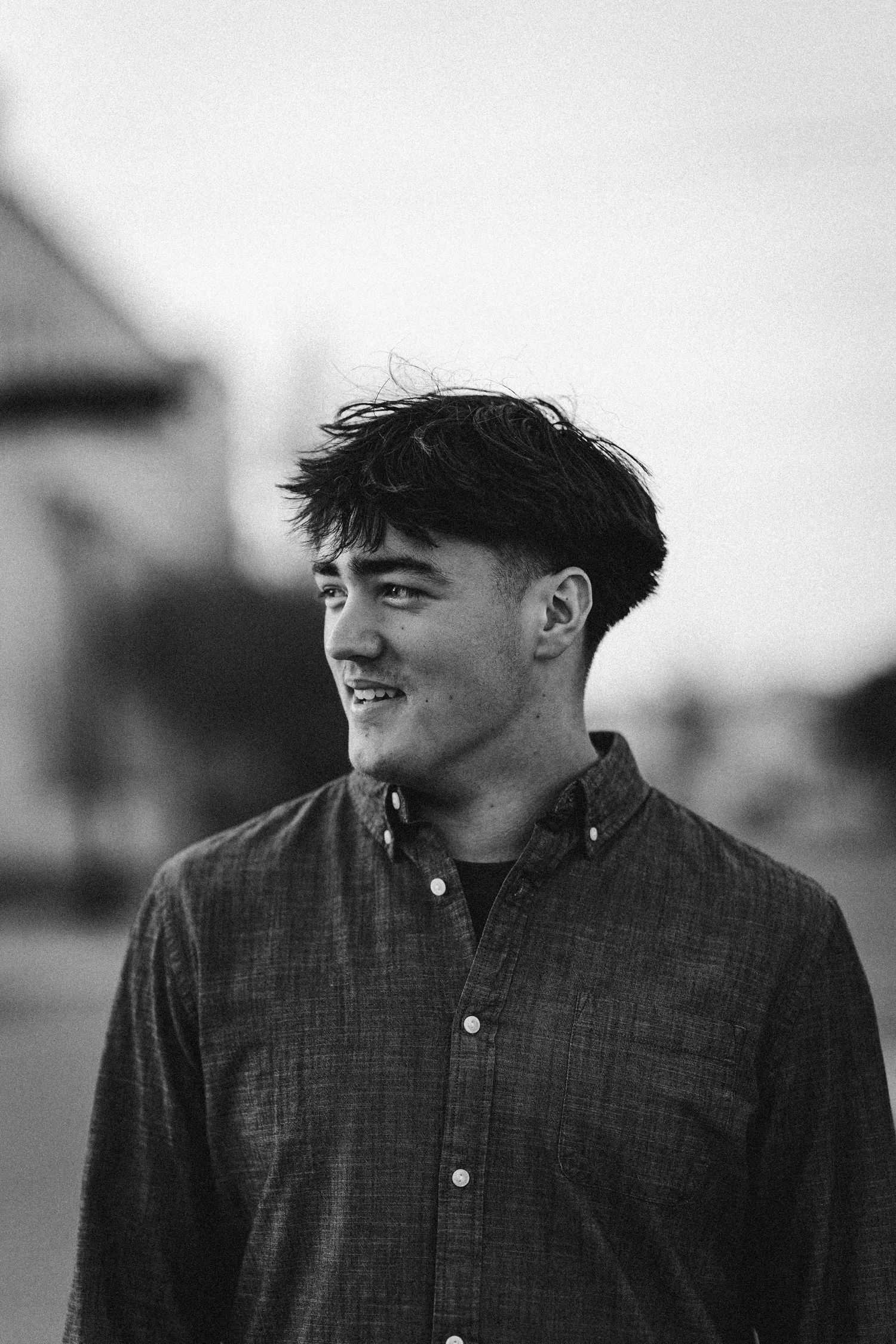 Black and white portrait of a young man with dark hair wearing a button-up shirt, smiling outdoors.