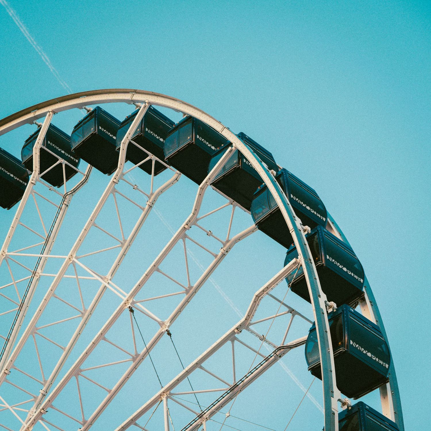 Close-up of a classic ferris wheel with gondolas against a clear blue sky at an amusement park.