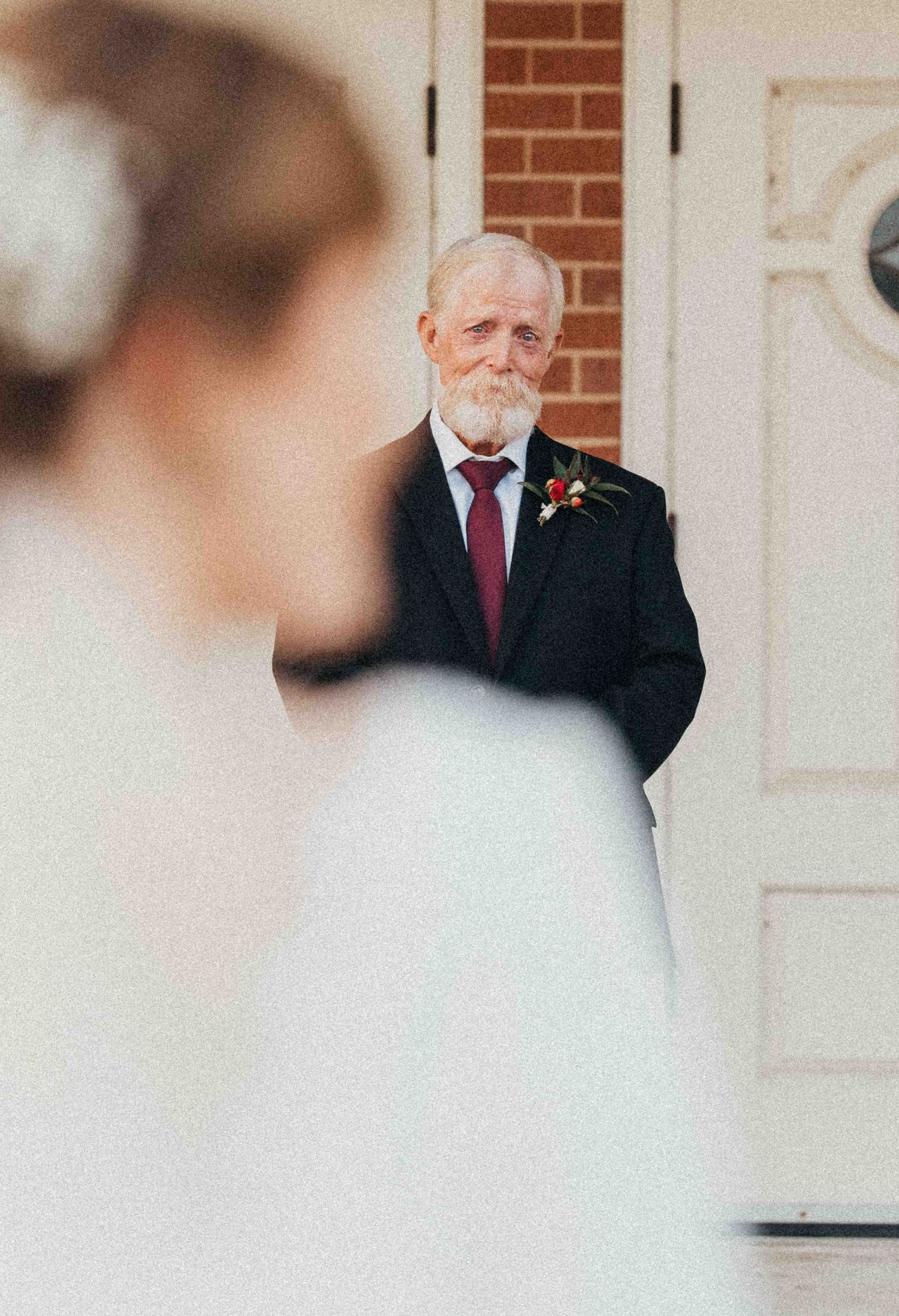 Emotional father seeing bride daughter in wedding dress for first look outside brick church.