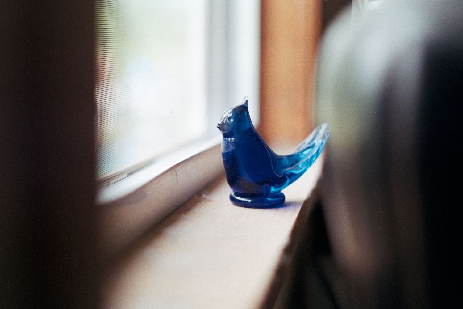 Blue glass bird figurine sitting on a wooden windowsill with soft natural light in the background.
