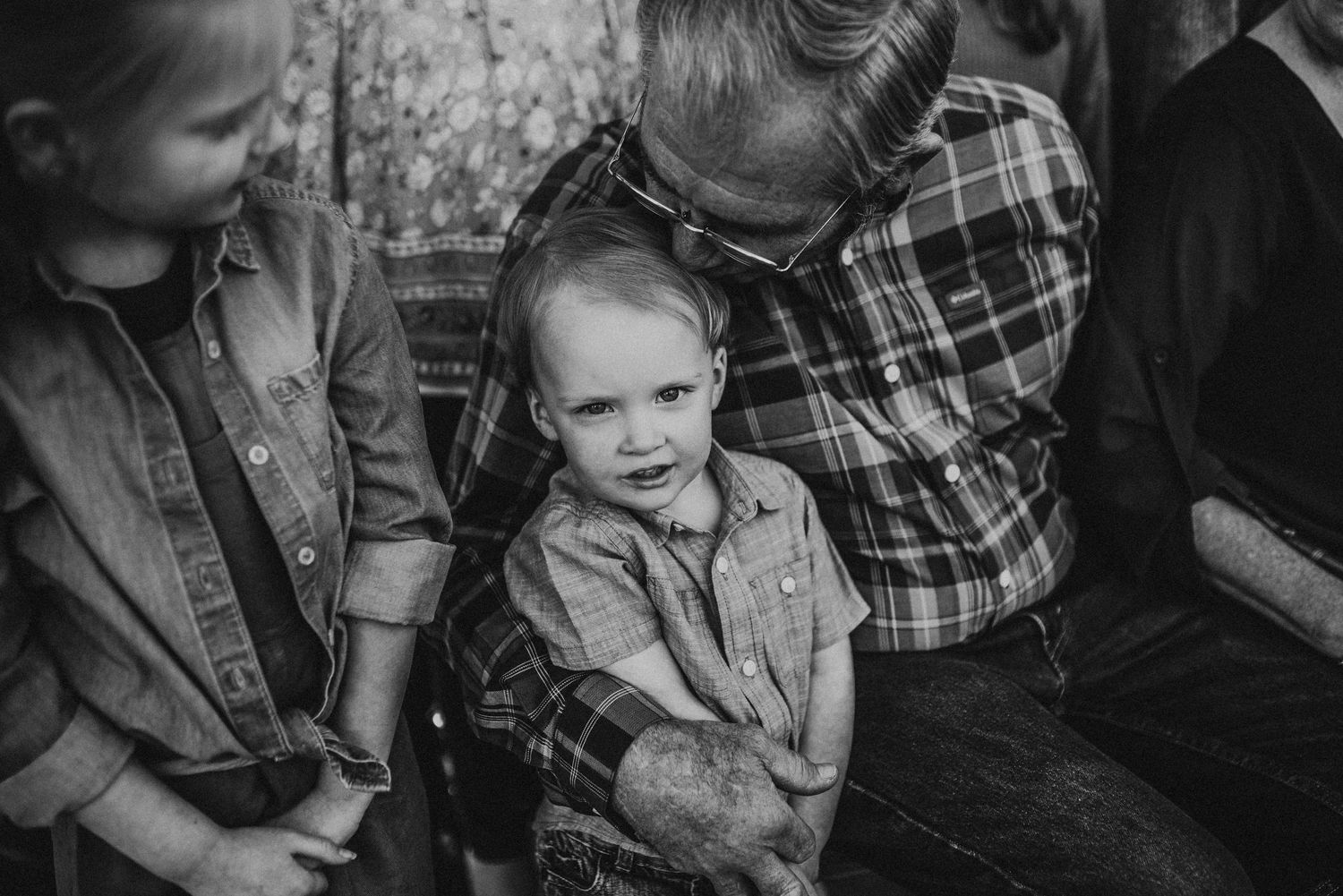 Black and white photo of a toddler boy sitting with an older man and child in a warm family moment.