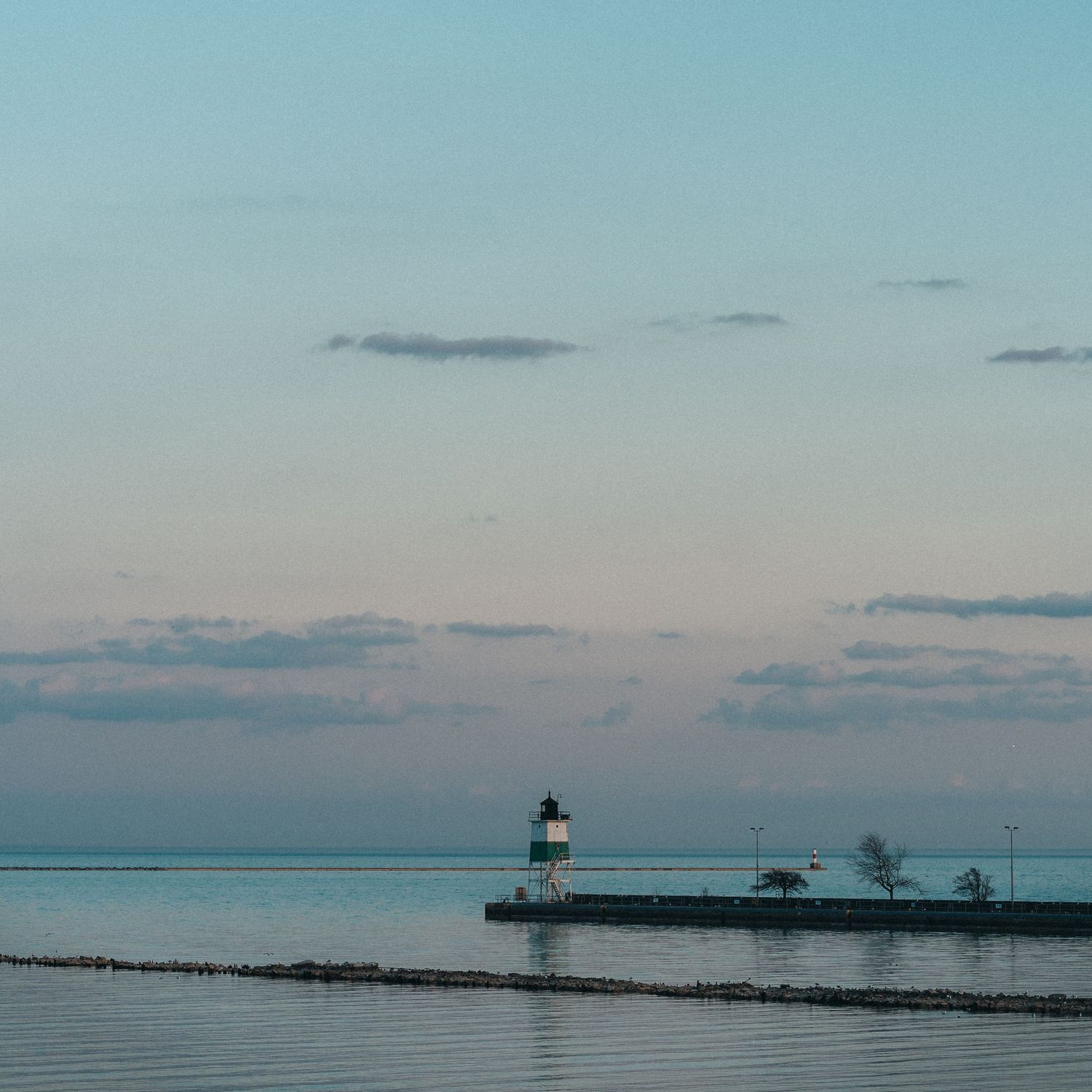 A serene lighthouse stands on a pier at dusk, surrounded by calm waters under a pastel pink and blue sky.