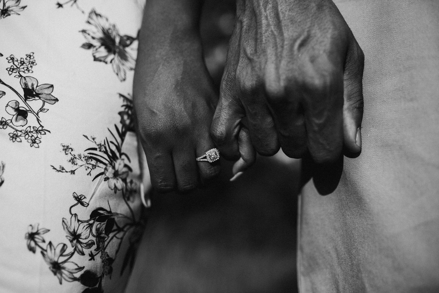 Close-up black and white photo of couple holding hands showing an elegant diamond engagement ring.