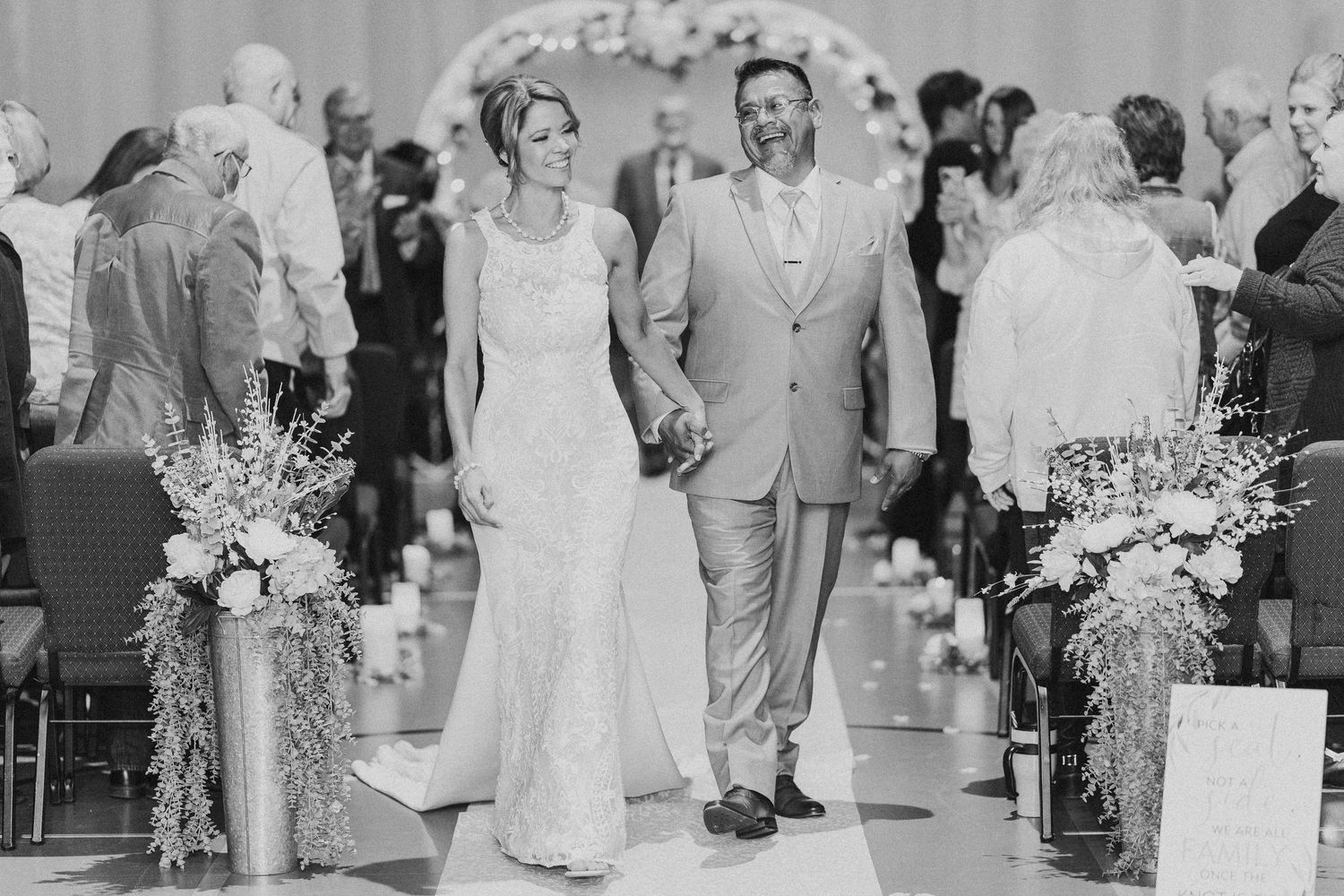 Black and white photo of a bride and groom walking down the aisle at their elegant wedding ceremony.