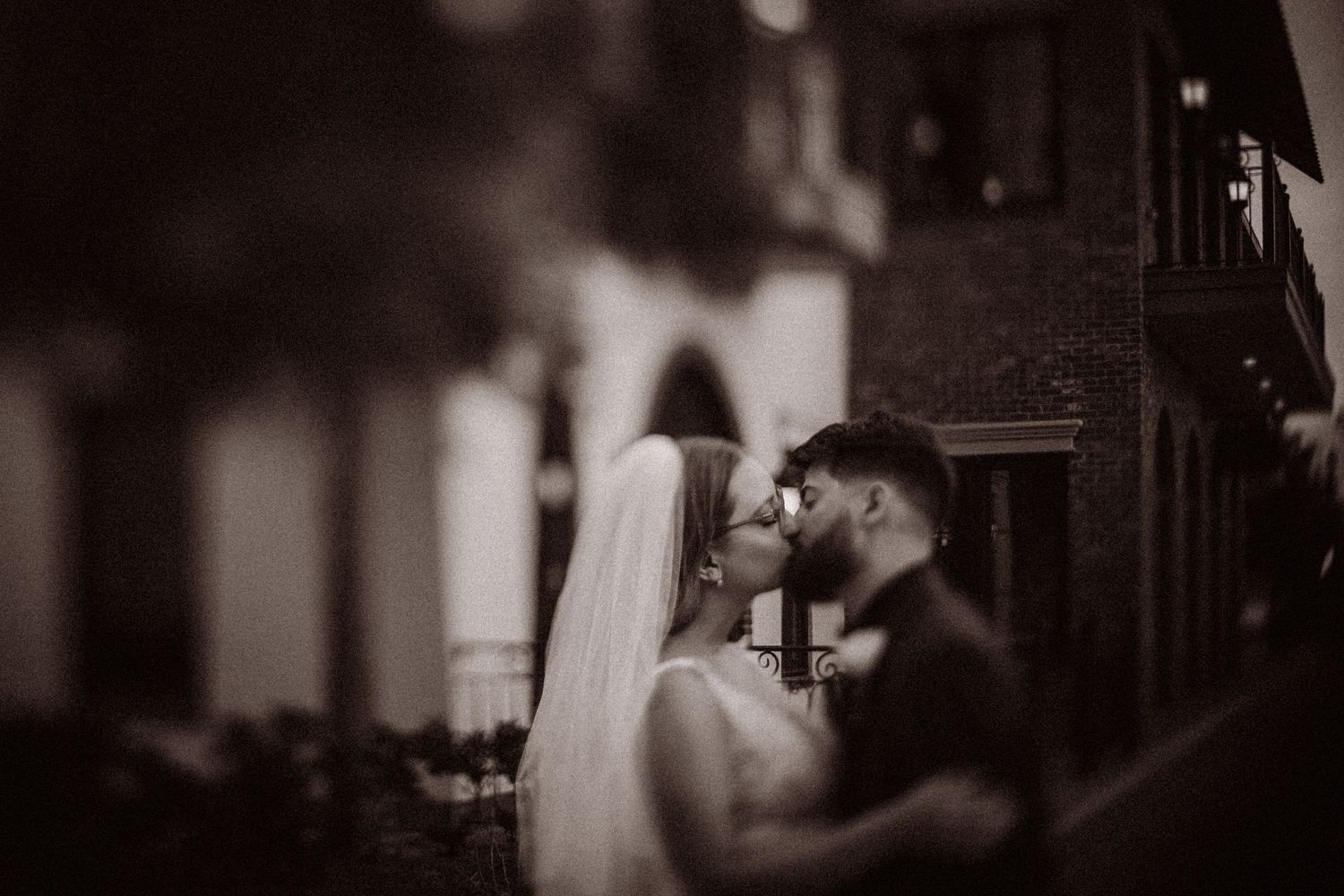 Black and white wedding photo of bride and groom sharing an intimate moment outdoors near a brick building.