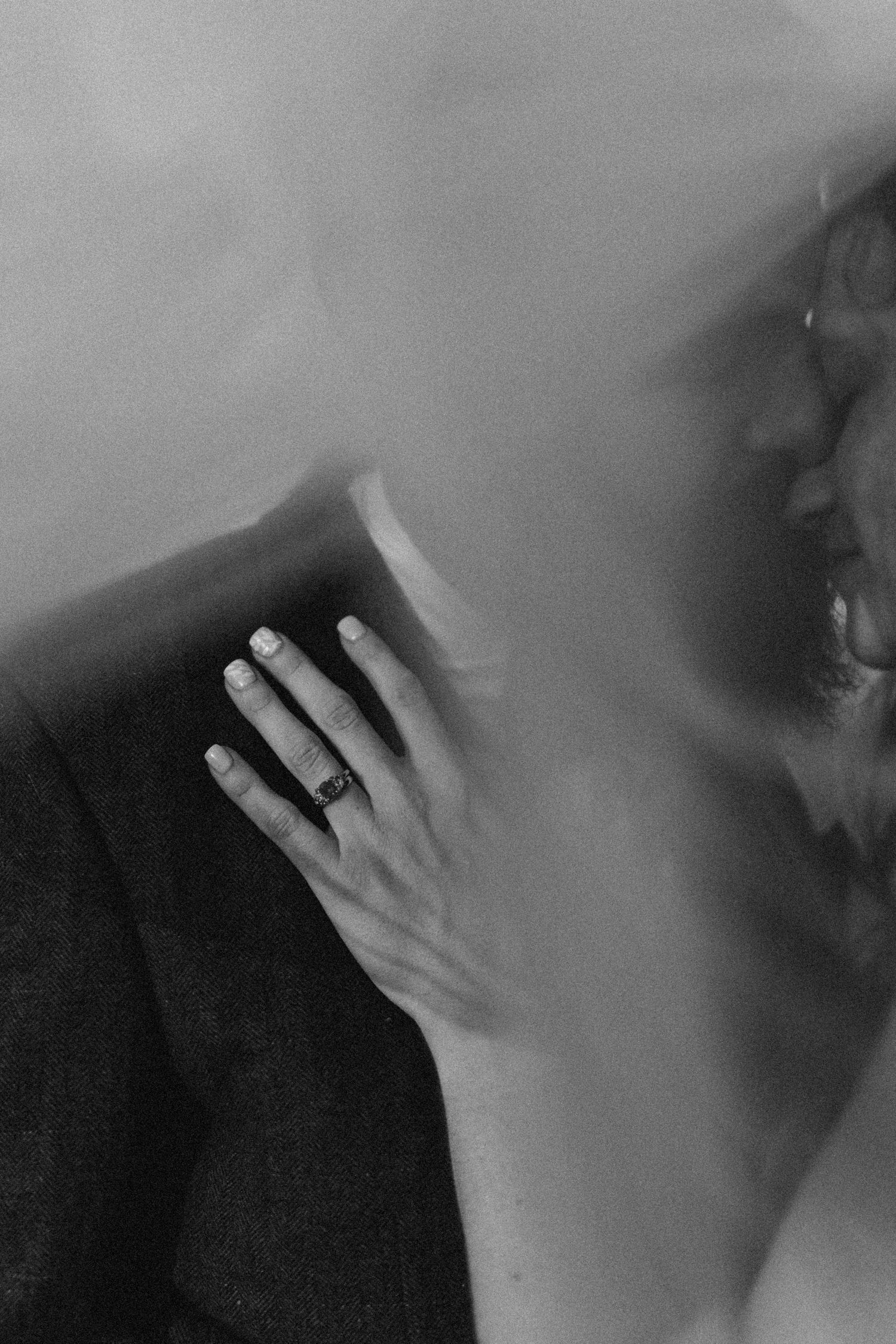 Black and white photo of a couple nearly kissing, woman's hand with ring resting on man's chest.