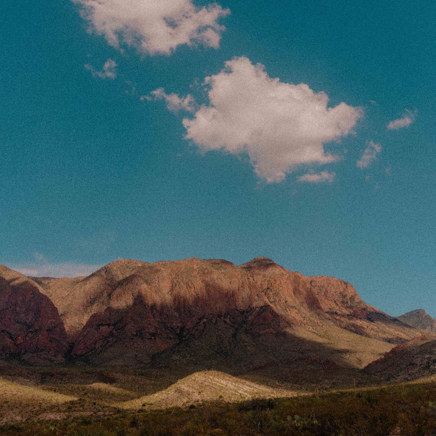 Dramatic red rock mountain landscape under vivid blue sky with white clouds in desert terrain.