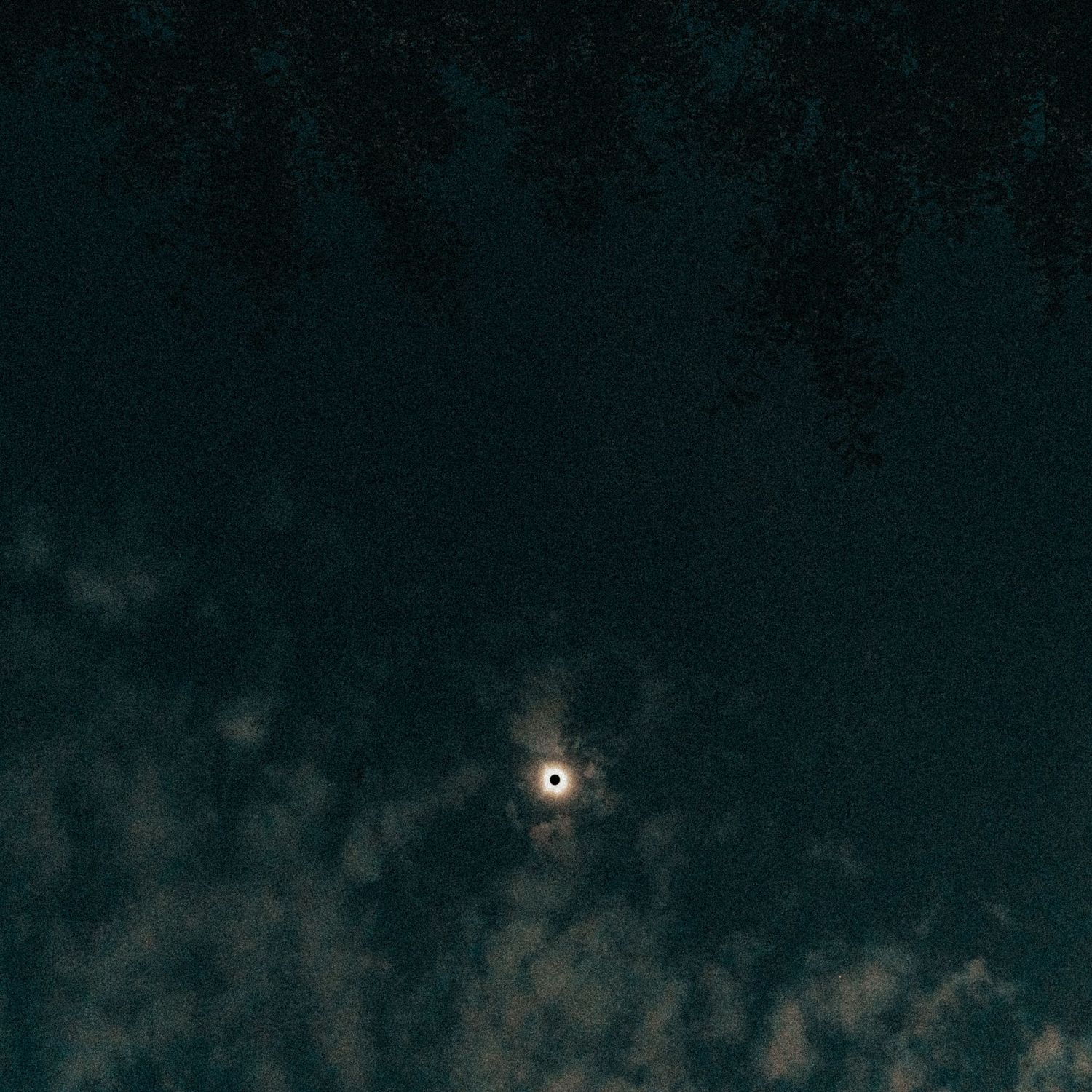 A total solar eclipse glows against a dark teal sky with wispy clouds, stars visible in the background.