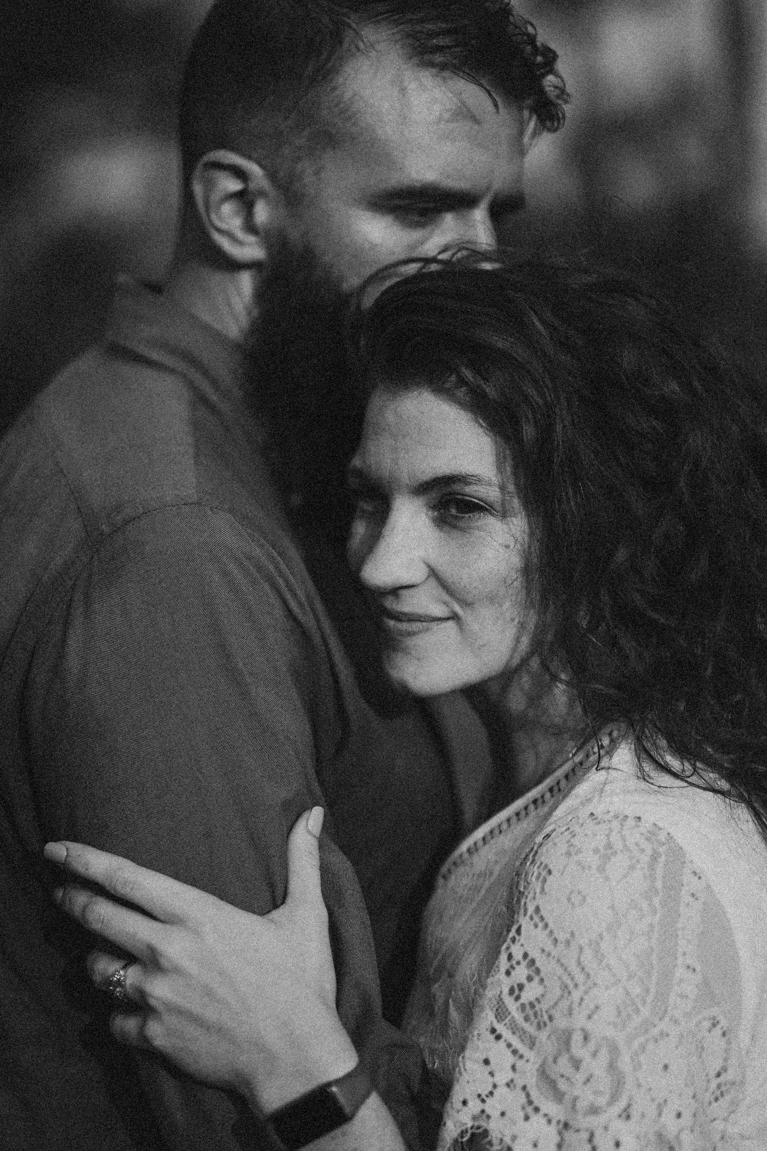 Black and white photo of a bearded man embracing a curly-haired woman in lace top, sharing a tender romantic moment.