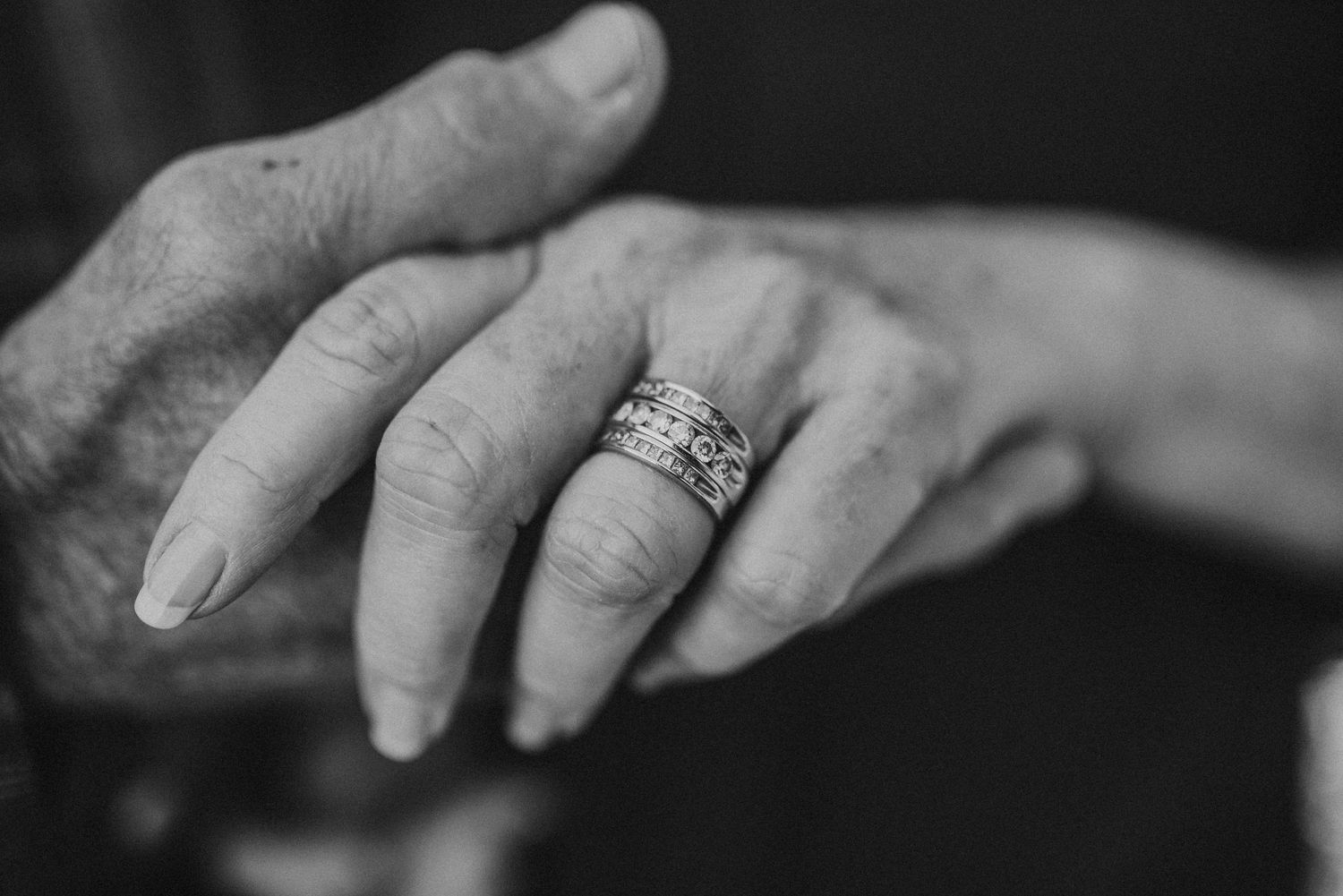 Black and white close-up of elderly hands with a diamond wedding band ring, symbolizing lasting love and commitment.