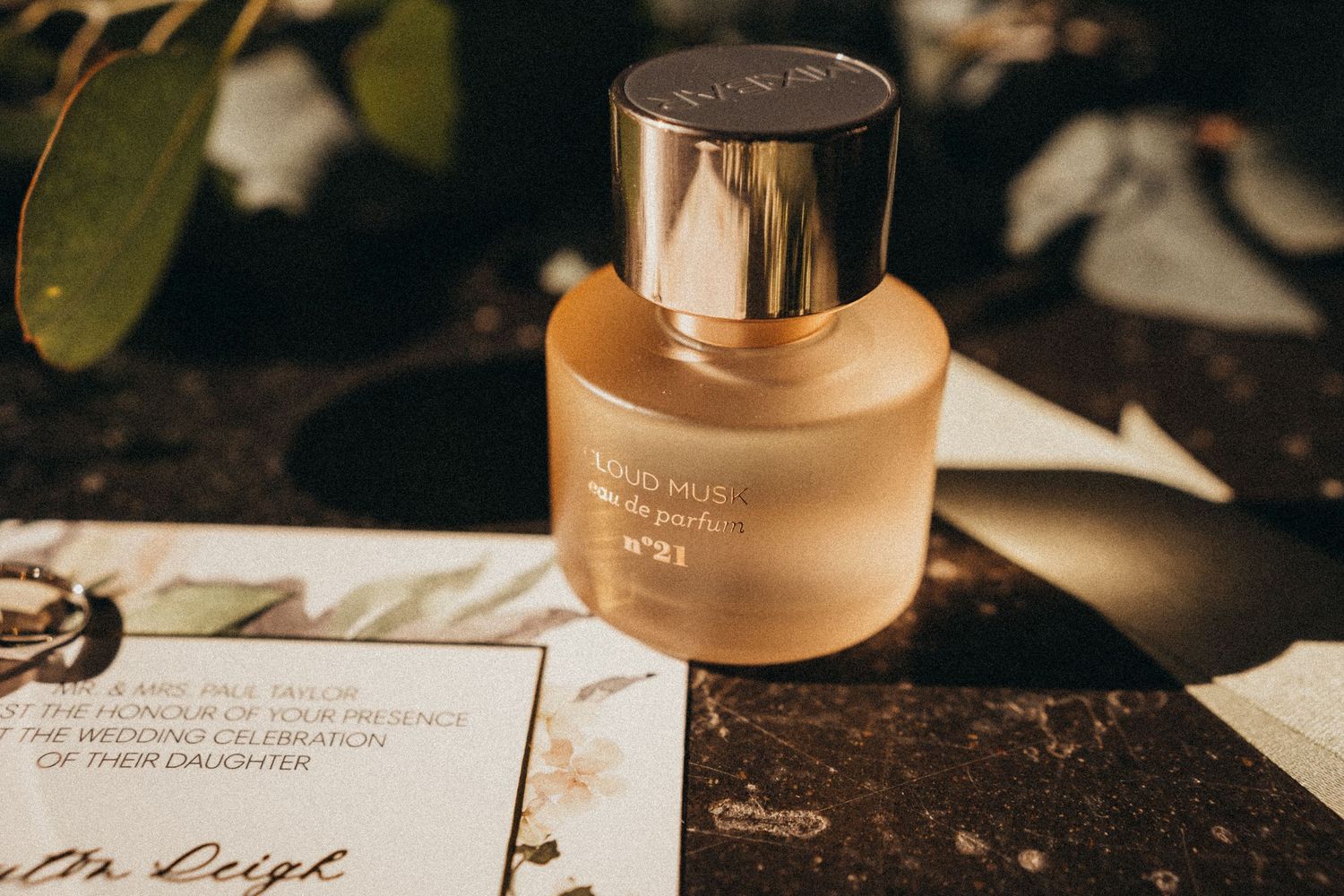 Elegant gold-capped perfume bottle on marble surface beside a wedding invitation card.