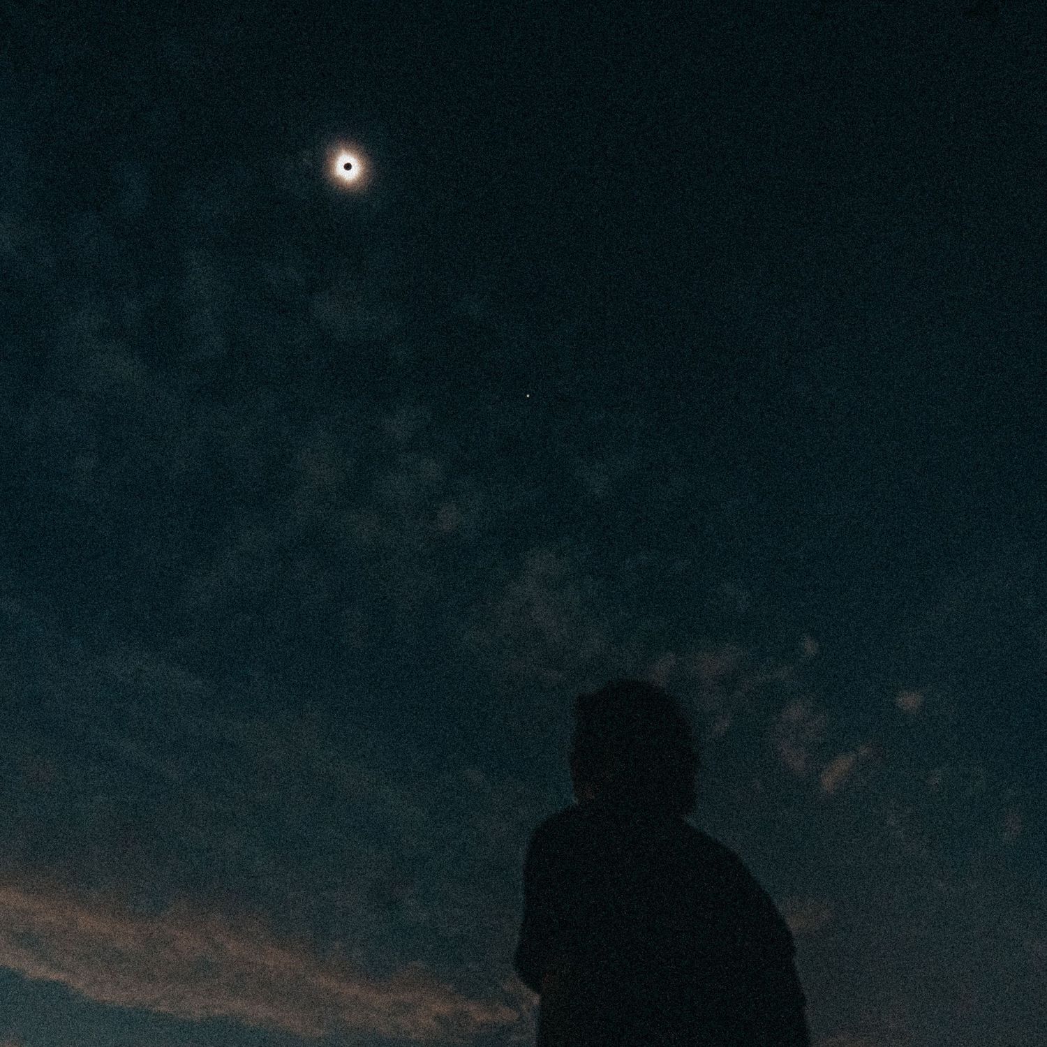 Silhouette of a person gazing at a total solar eclipse in a dramatic dark blue cloudy night sky.