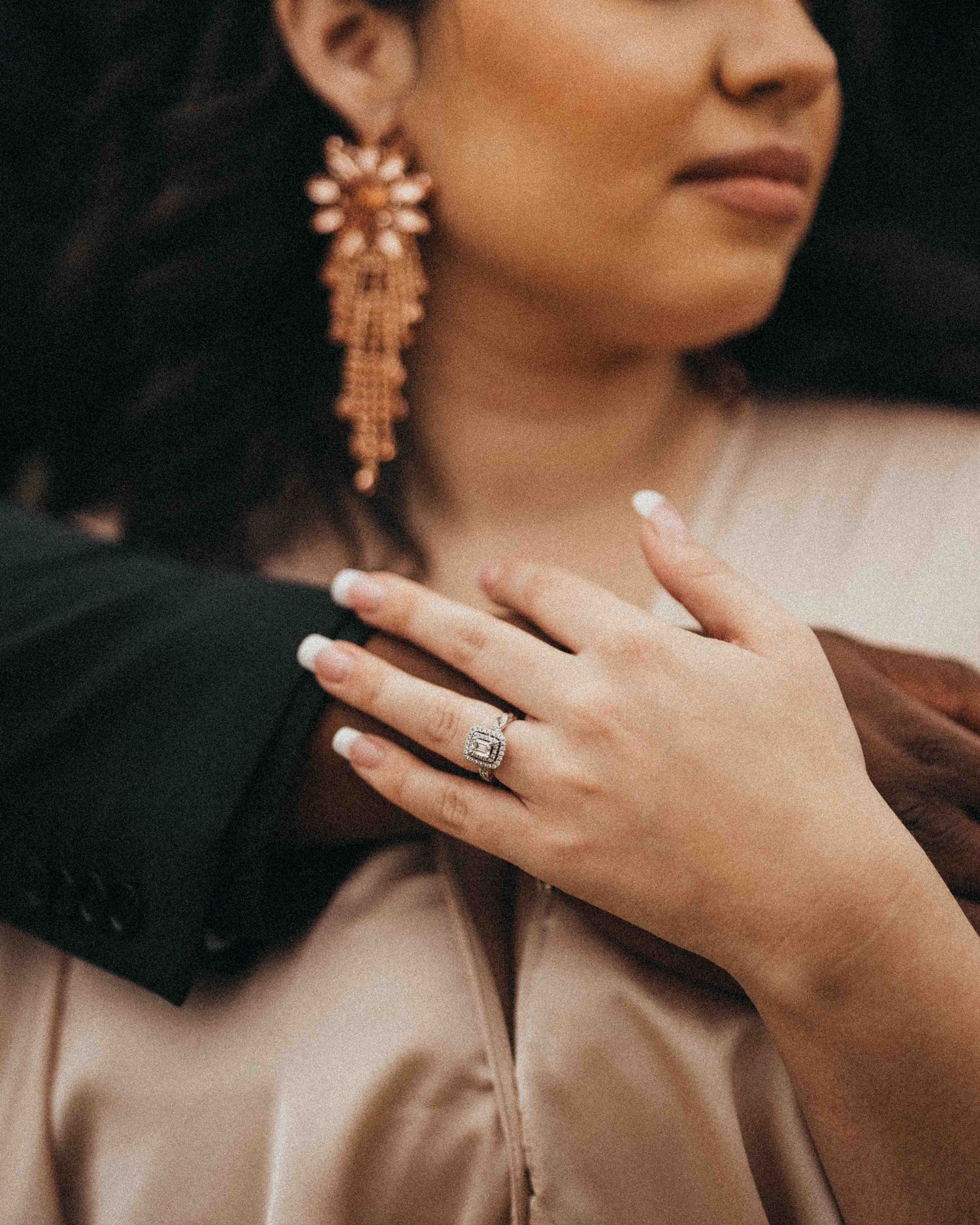 Close-up of a woman wearing a sparkling chandelier earring and a diamond ring with French manicured nails.