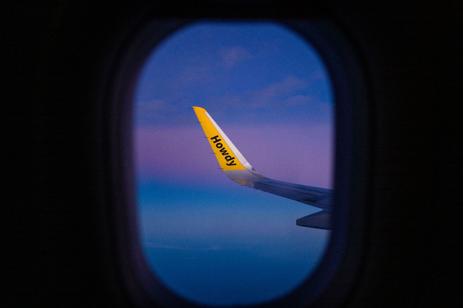 View from airplane window showing a yellow wing tip against a stunning pink and blue twilight sky.