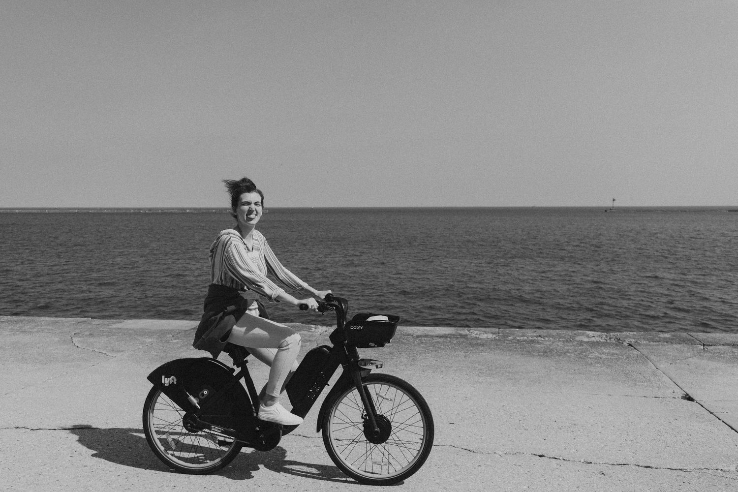 Woman riding a bicycle along a seaside promenade on a sunny day, black and white photo.