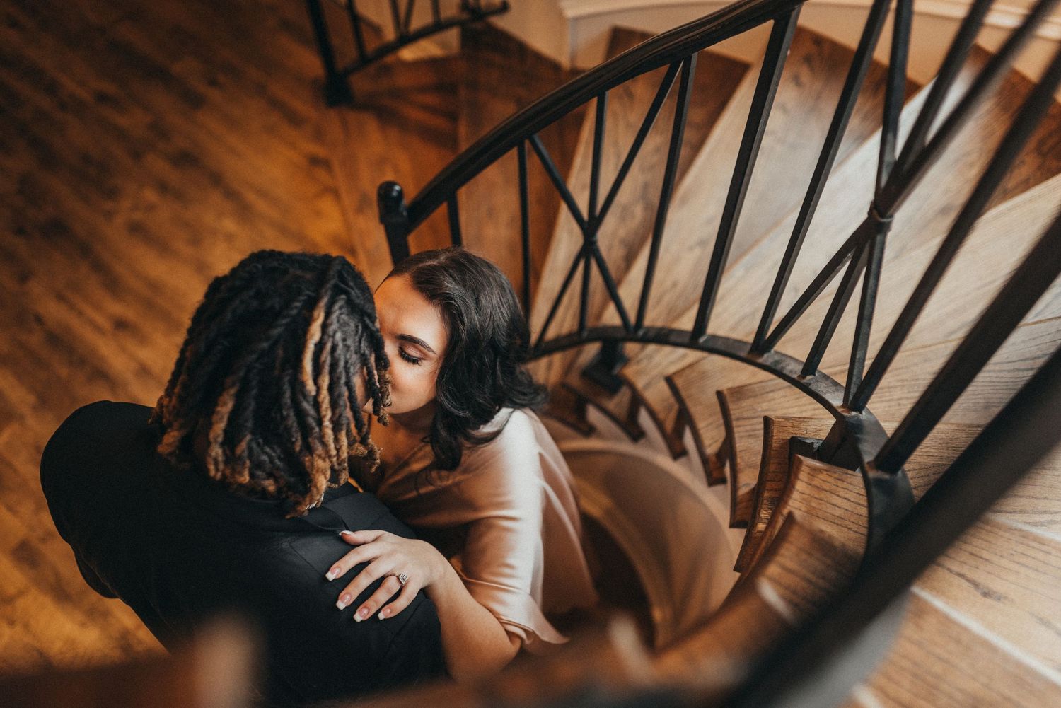 Overhead view of a couple sharing a tender kiss on a wooden spiral staircase.