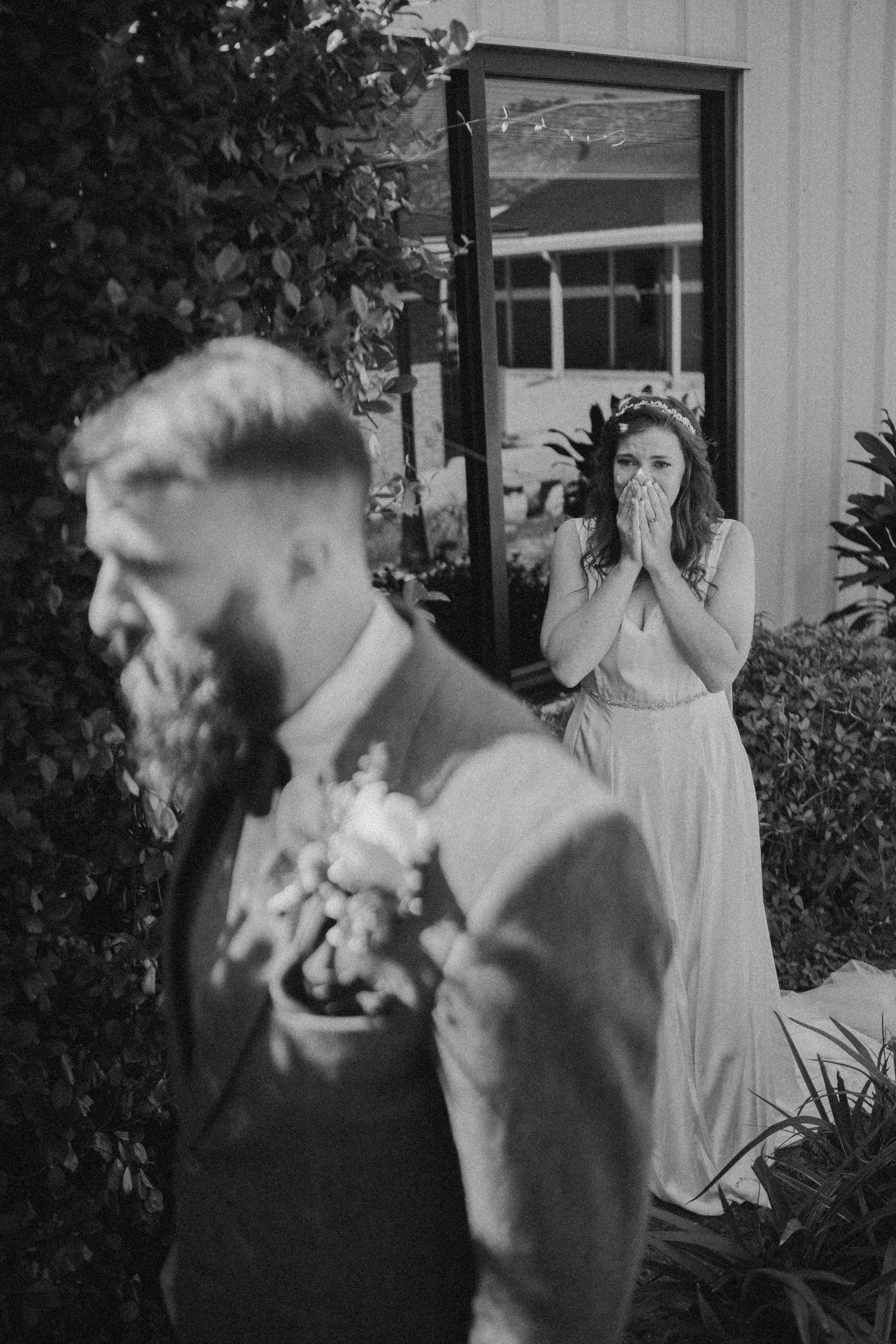 Emotional bridesmaid covers mouth in surprise seeing groom outdoors in candid black and white wedding photo.