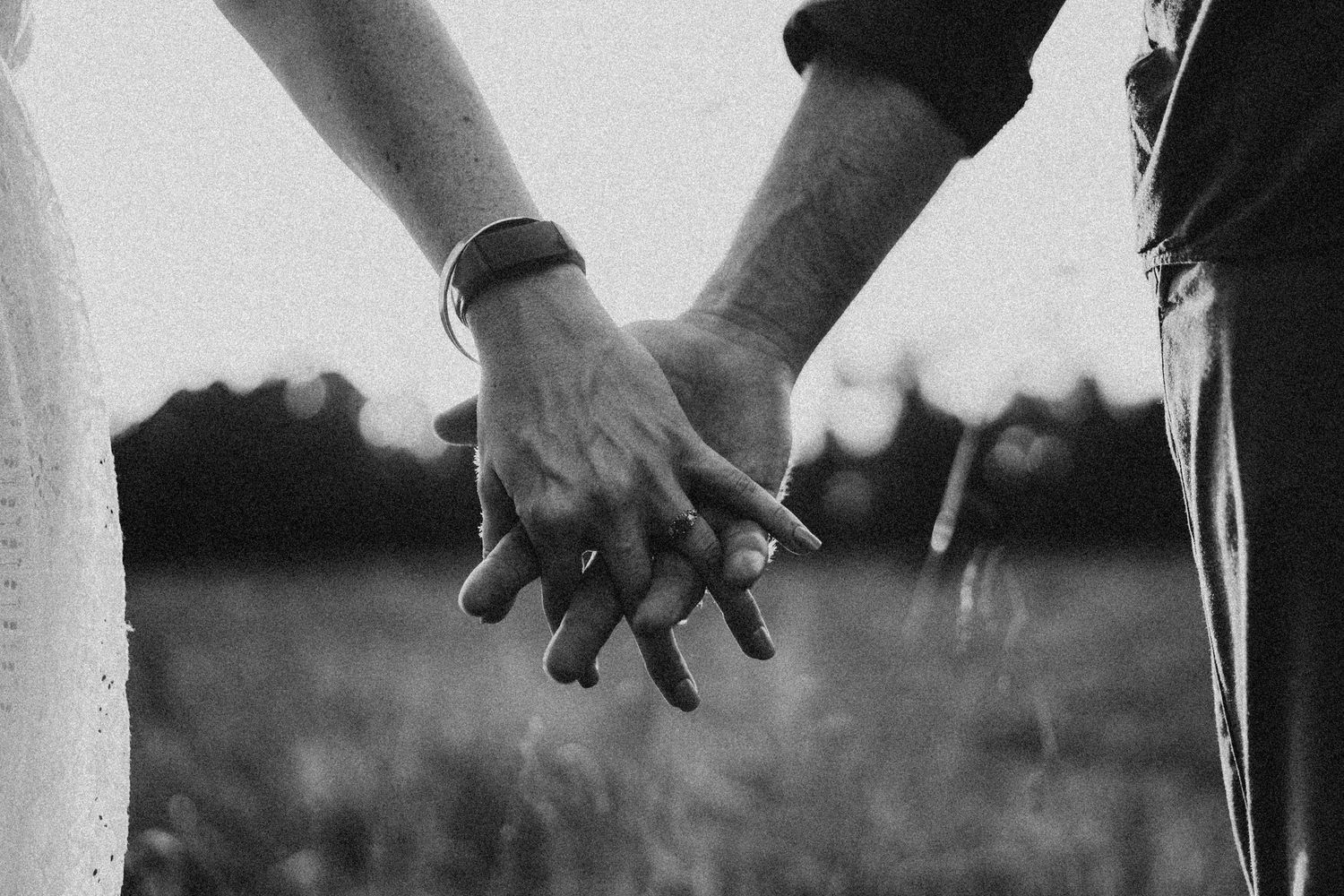 Black and white photo of a couple holding hands in a field, symbolizing love and togetherness.